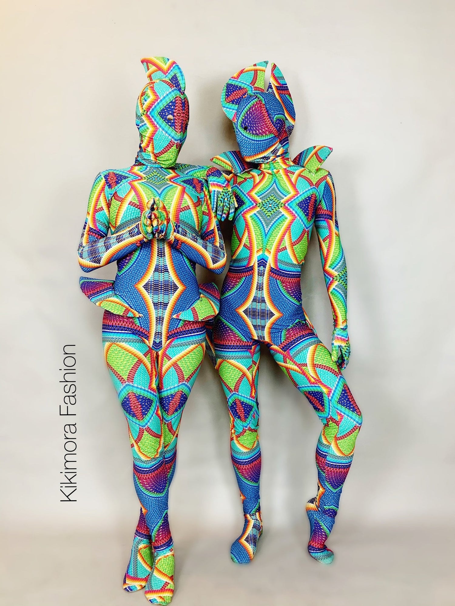 Two people in colorful, geometric-patterned bodysuits stand posing against a plain background.