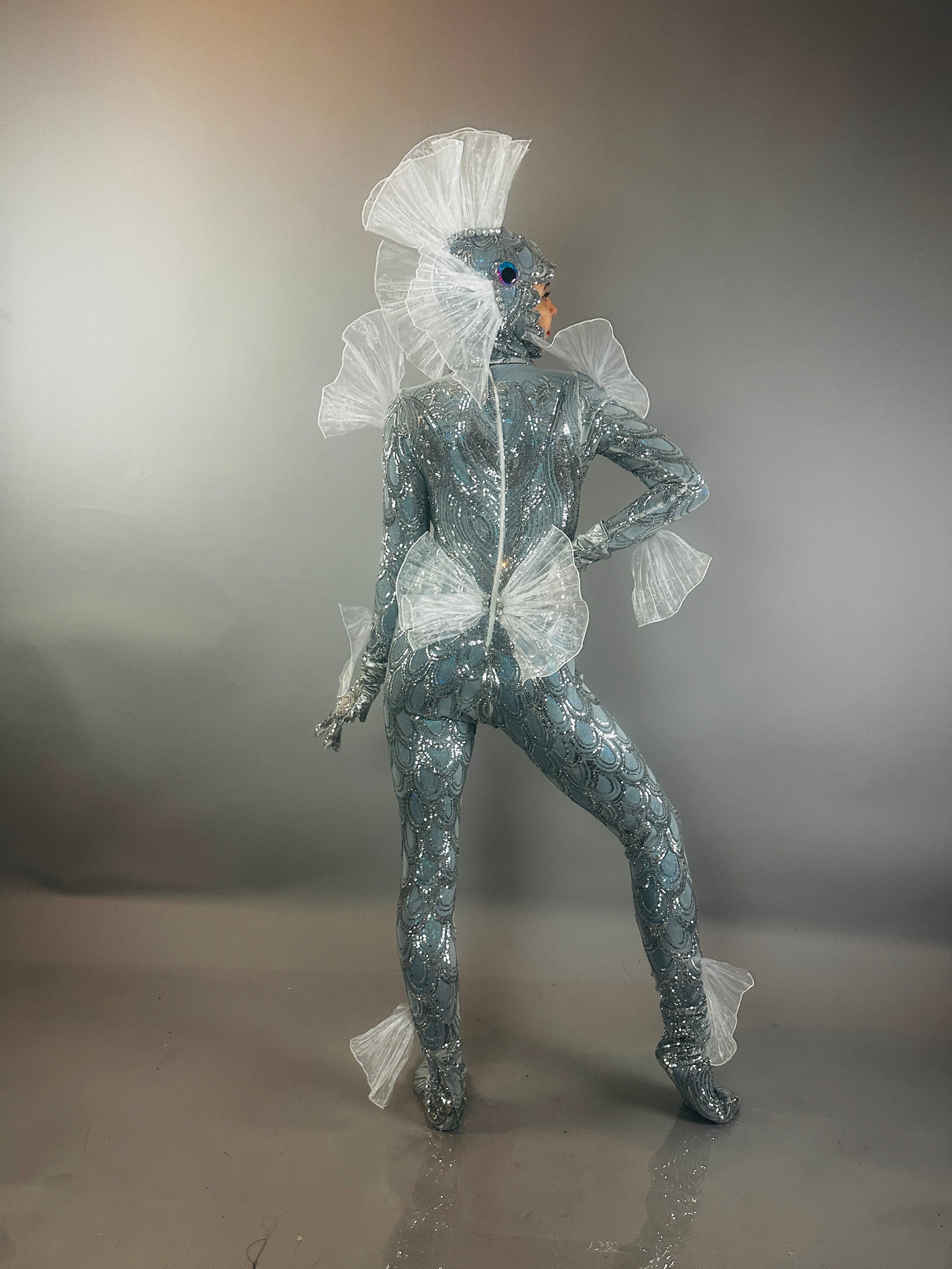 The Sea Creature is a silver, shiny, textured bodysuit with fins that creates a dazzling, futuristic aquatic look—a wearable sculpture and striking costume.