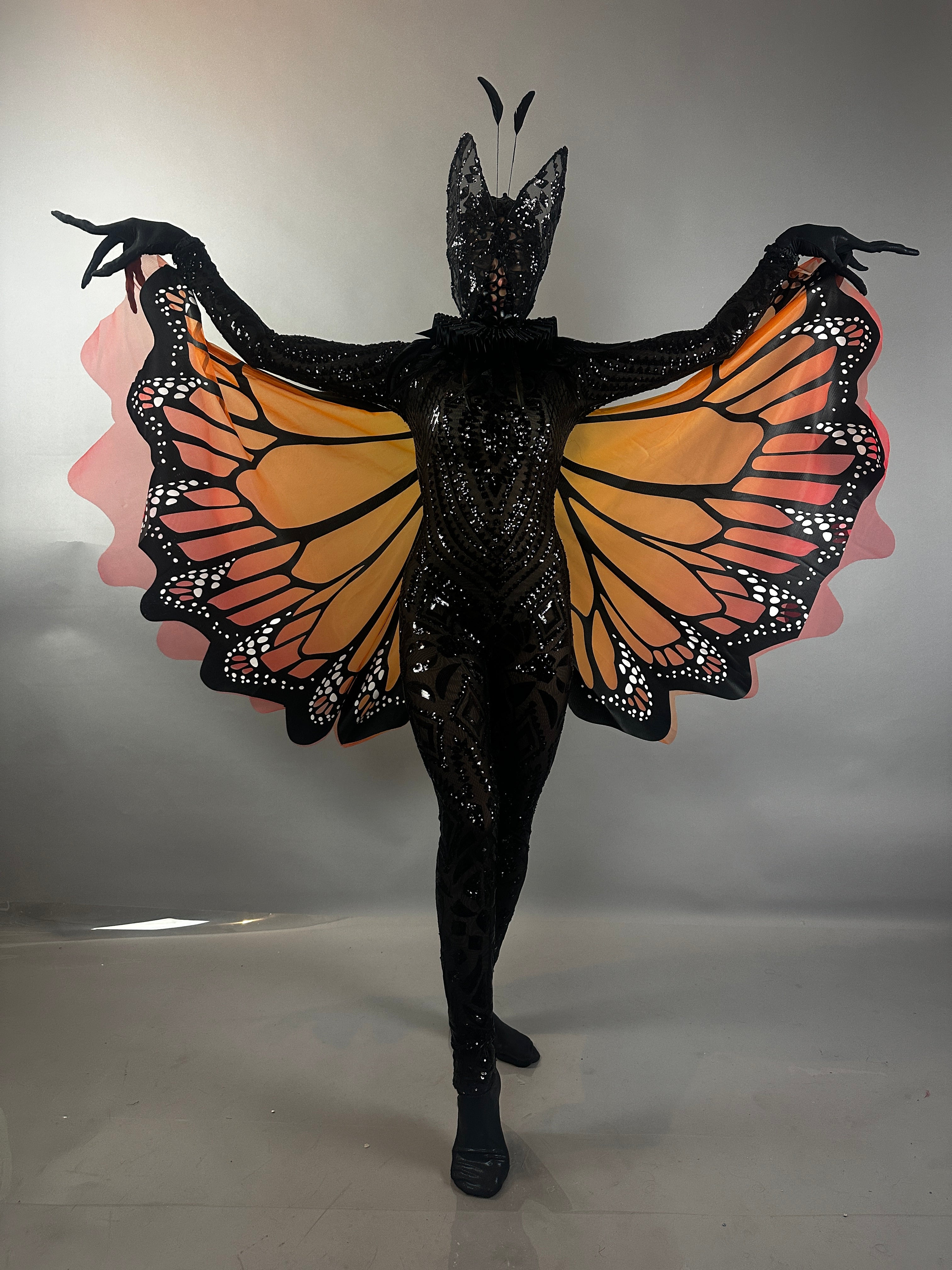 Model wearing the Black Sequin Full Costume Butterfly, which features striking orange and black wings and antennae, poses against a plain background—an eye-catching piece of wearable art.