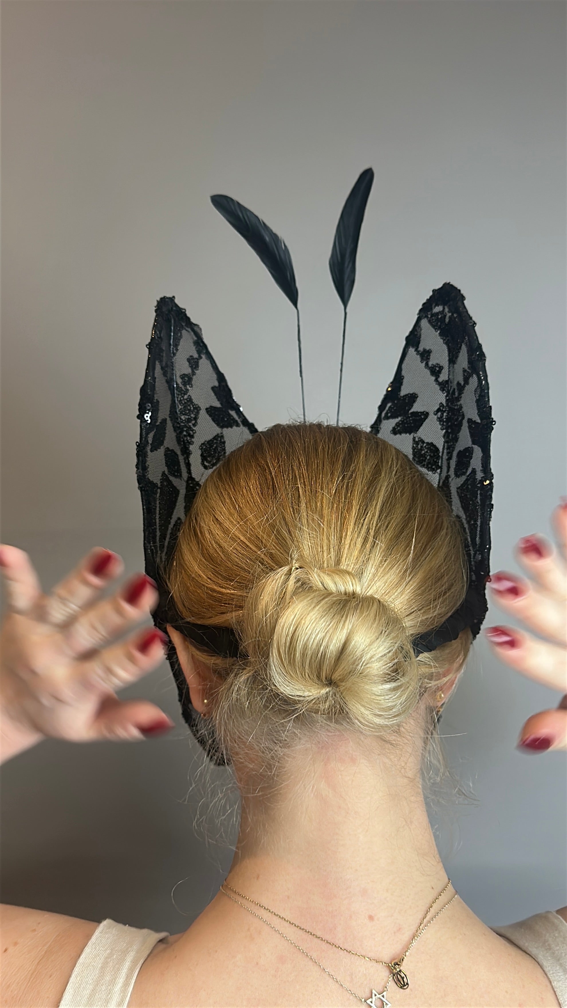 A person with a blonde bun wears a Butterfly Headpiece—an open face, black lace holiday costume accessory—hands raised near their head to display this festive hat.