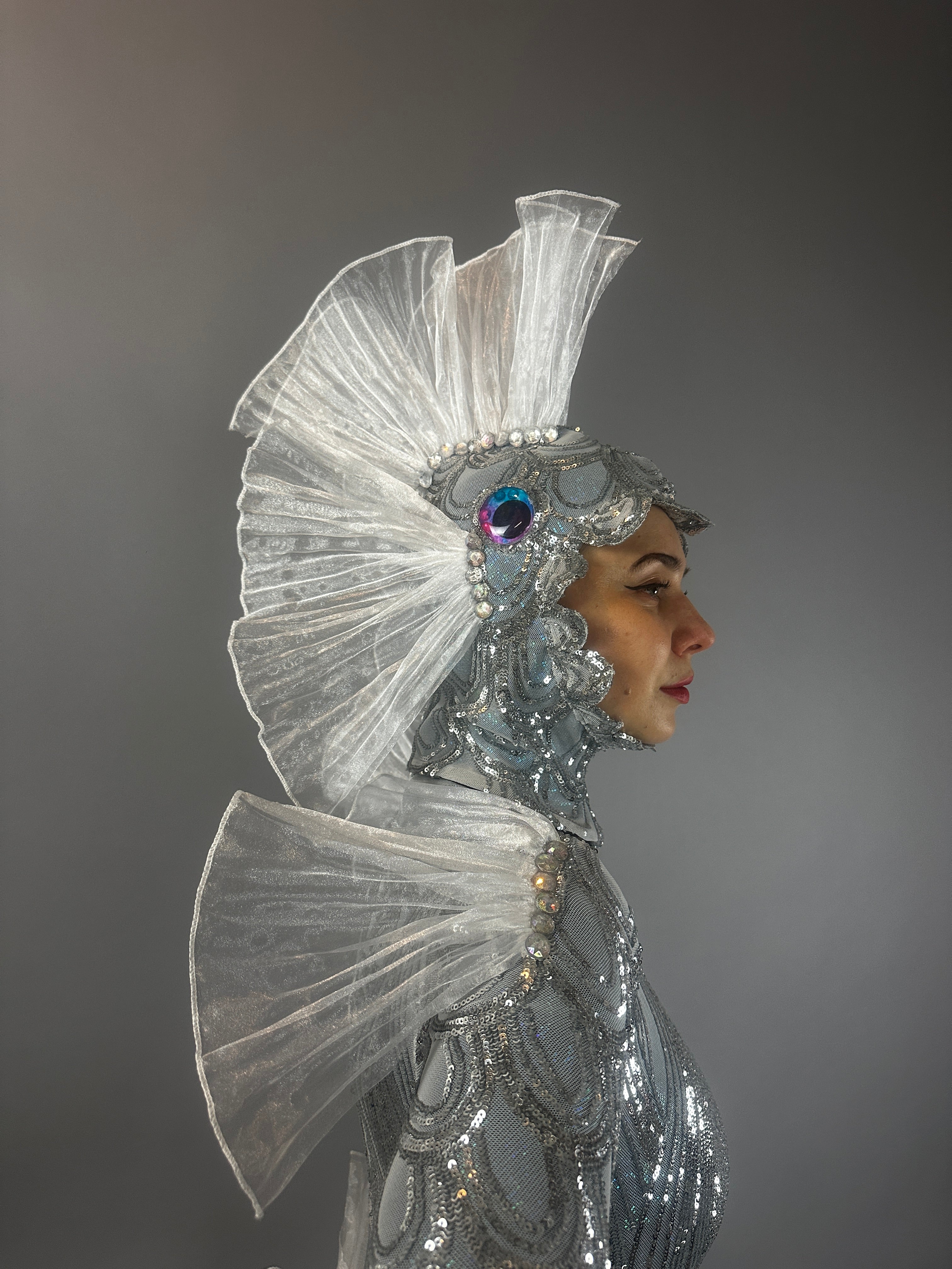 Model is wearing the Sea Creature costume, featuring a shiny silver finish, fin-like headpiece, and iridescent details—a stunning display of couture design.