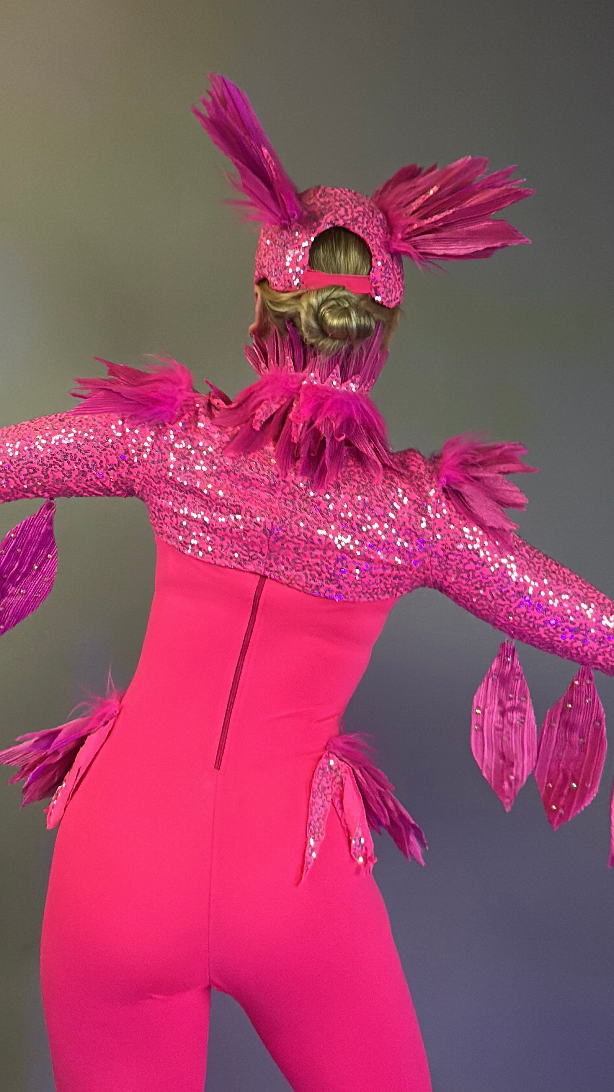 Person in the Pink Bird Full Costume for Aerial and Dancers—vivid pink, sparkling, with feathers and outstretched wings—faces away from the camera, perfect for dazzling stage performances.