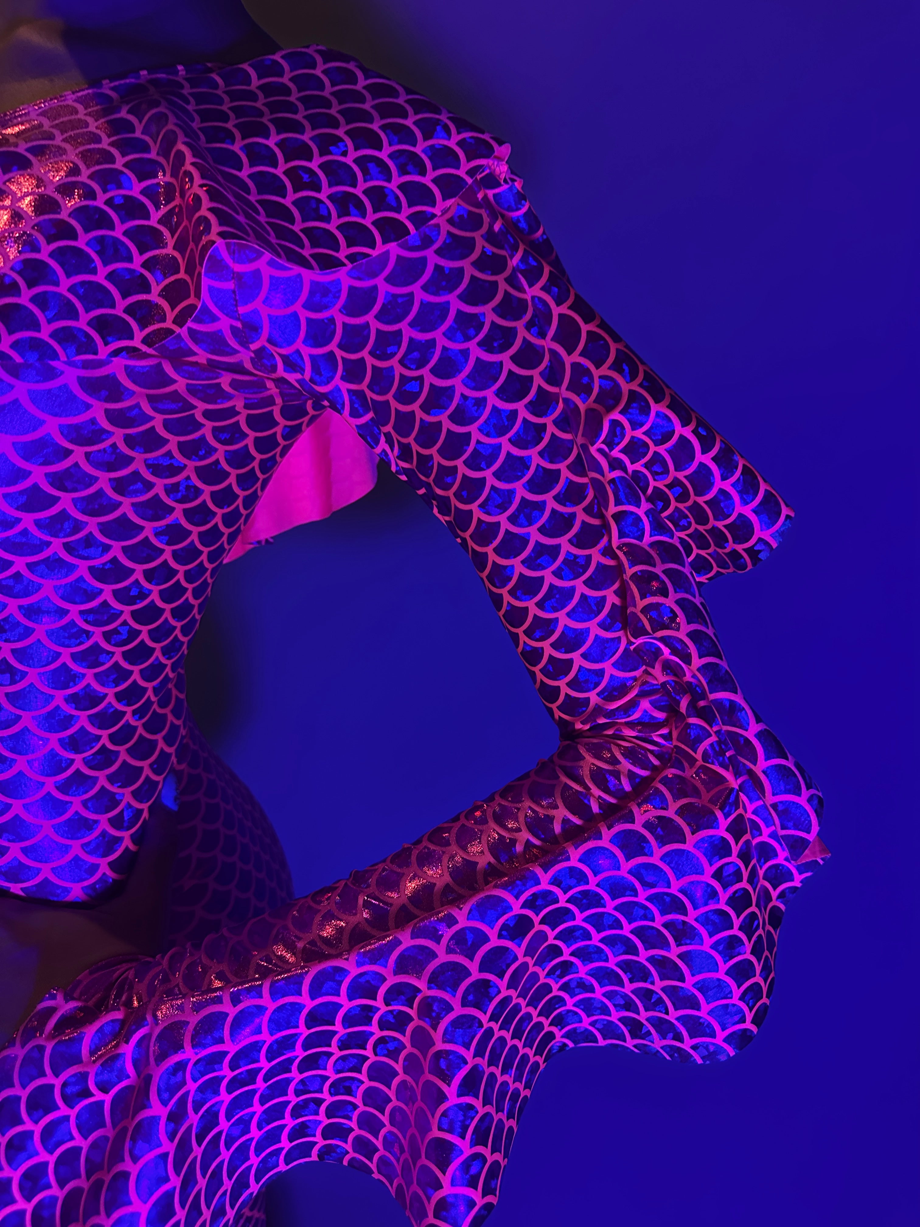 A person wears the Red Ruffle Catsuit featuring an off-shoulder spandex design and asymmetrical ruffles, posing against a blue background.