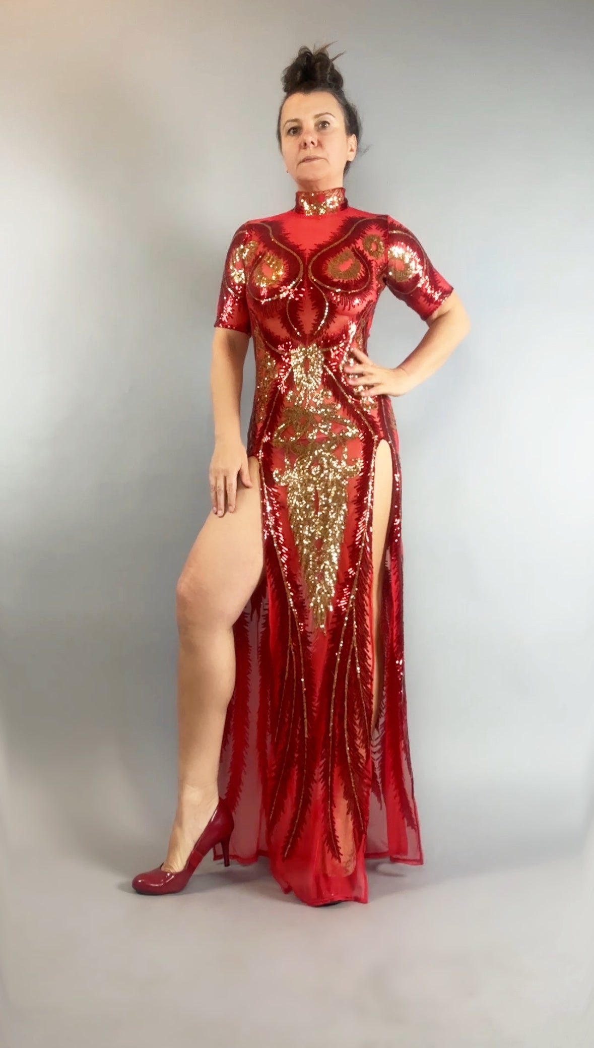 Confident woman in a Red and Gold Sequin Sheer Dress, sleeveless, styled with hand accessories and matching heels, striking a stylish pose.
