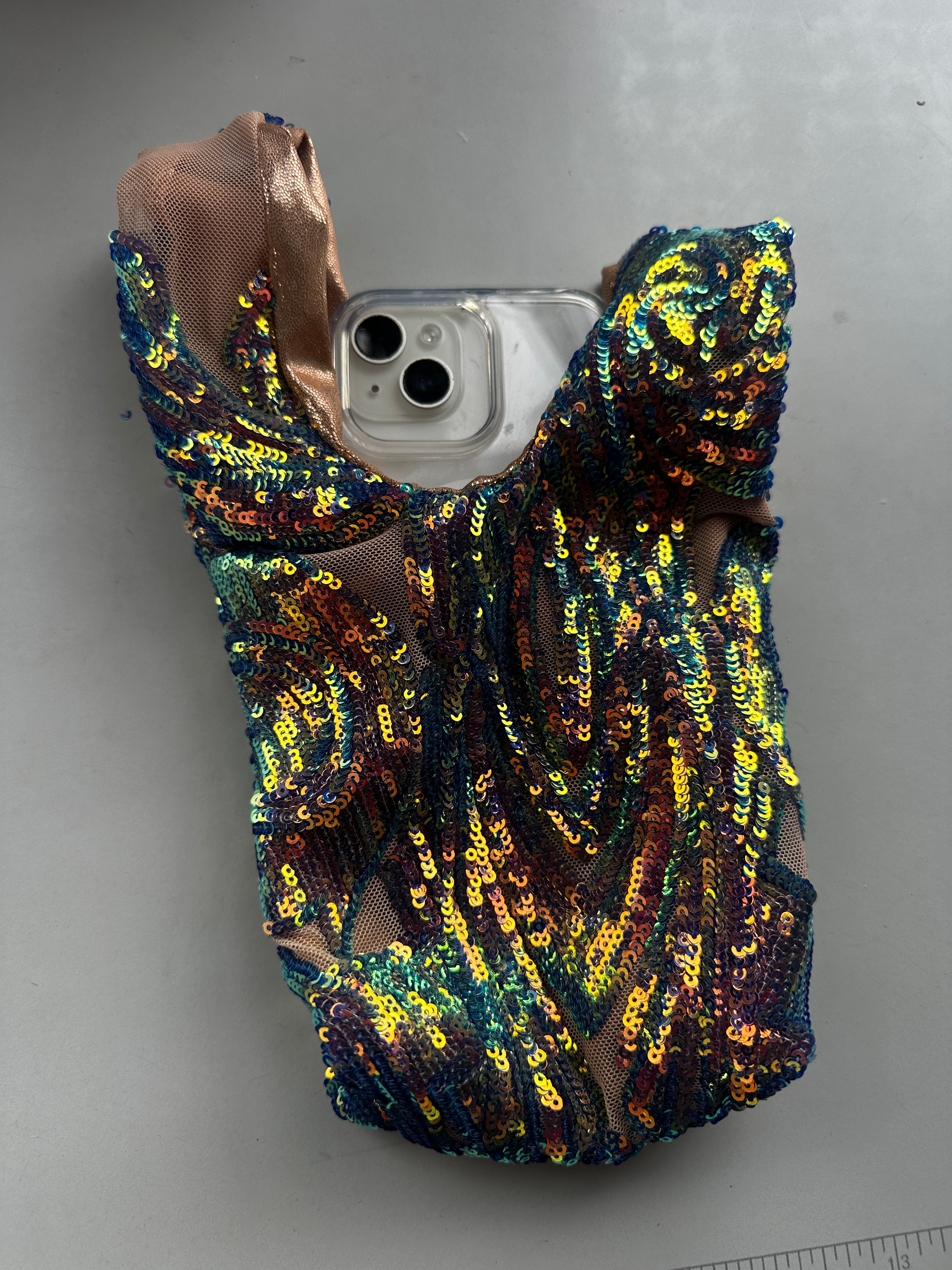 A phone partially covered by a handcrafted reversible sequin mini tote, a sustainable fashion accessory featuring colorful sequins and mesh, reminiscent of handmade Miami bag style.