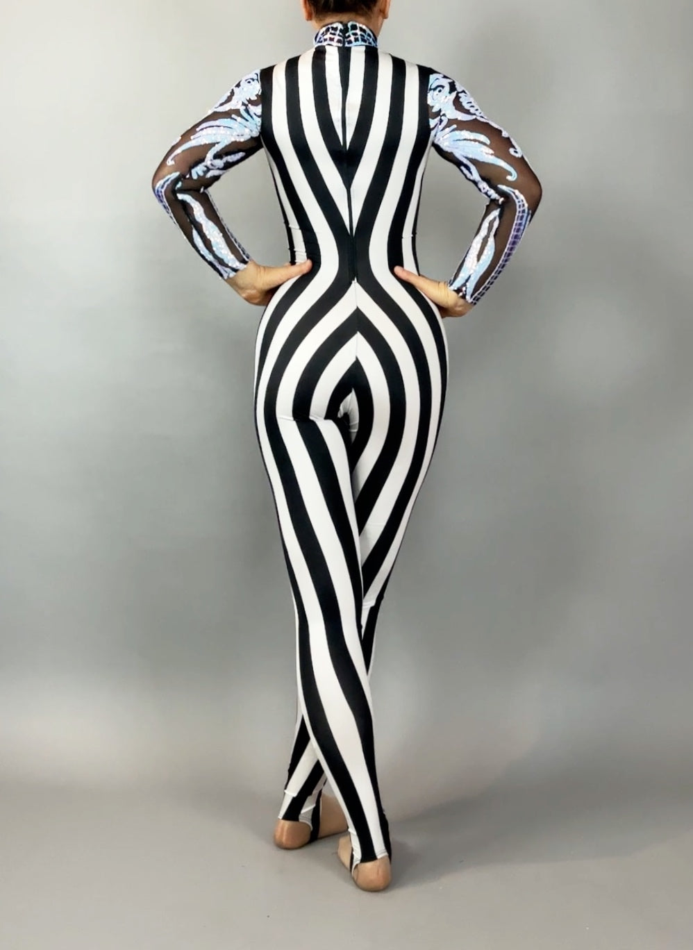 A person wearing the Glamorous sequins Stripes Catsuit costume, featuring black and white stripes with sheer patterned sleeves and a sequined leaf design, is standing with their back to the camera.