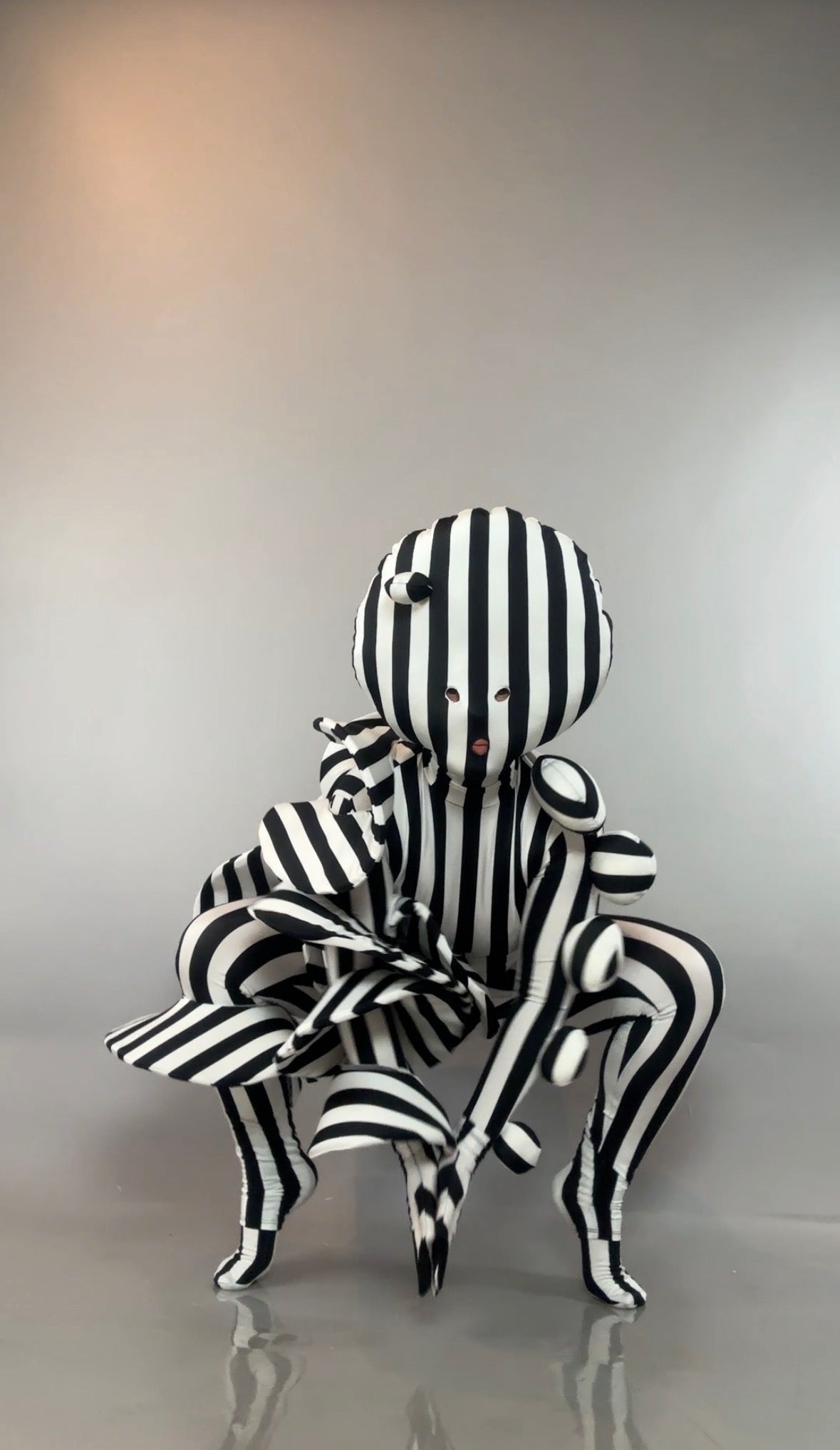A person in a Black and White Striped Creature Costume with Sculptural Details, featuring a round, sculpted headpiece.