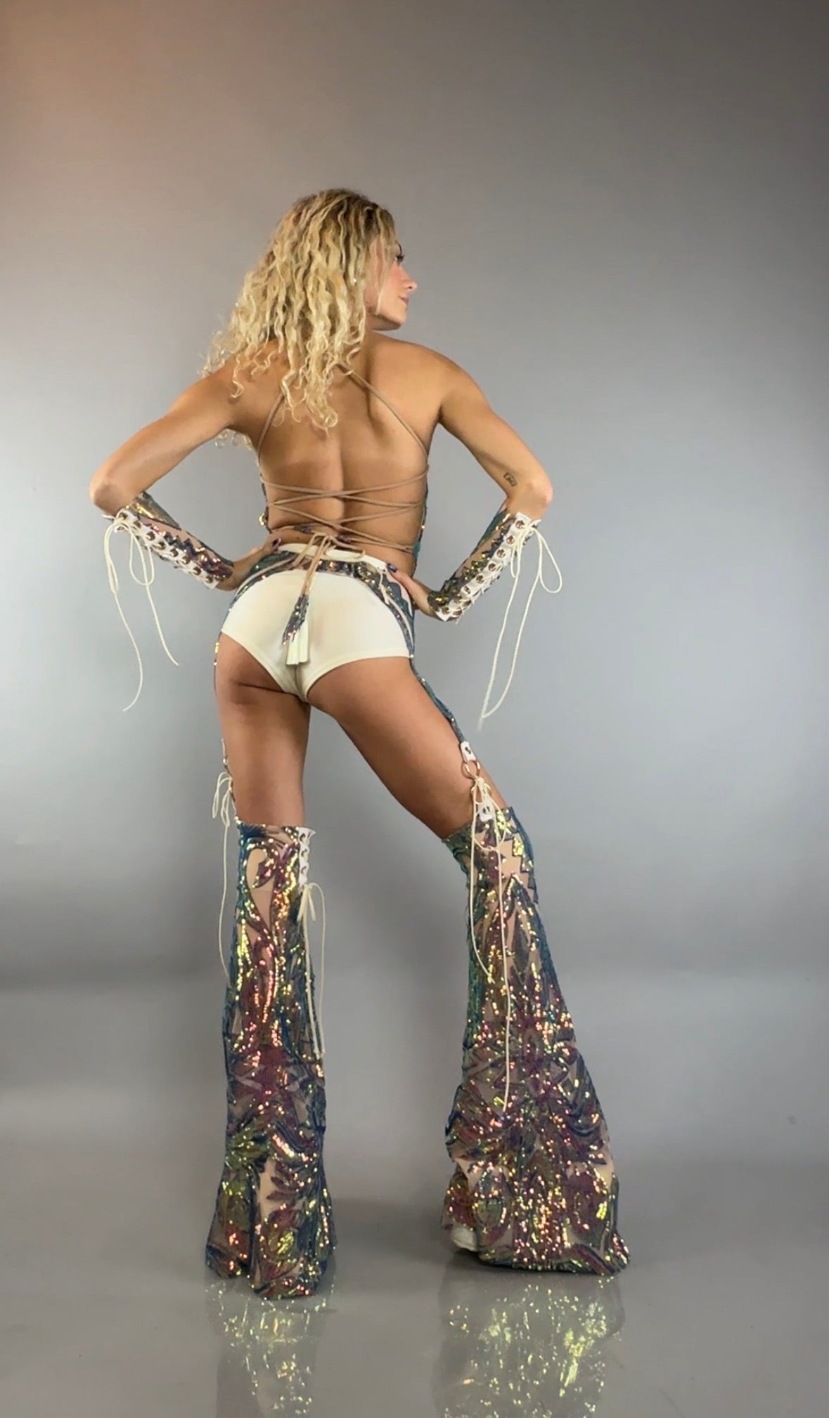 Woman models the Chaps Pants, Laced Top, and Sequins Festival Costume Setâposing with hands on hips and facing away from the cameraâfor a bold, custom dancewear look that shines on stage.