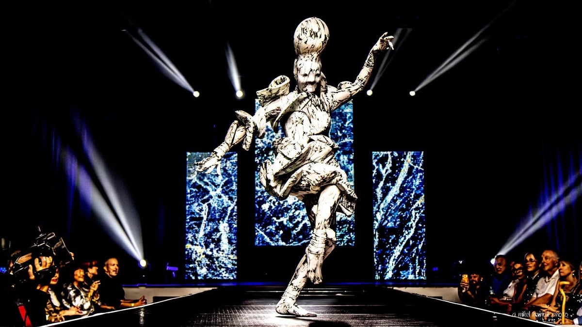 A model in an avant-garde costume poses dramatically on a lit runway, their marble print spandex Mushroom Creature Costumeâan artistic fungus-inspired full body suit with UV glowâcatching the light as the audience sits captivated on both sides.