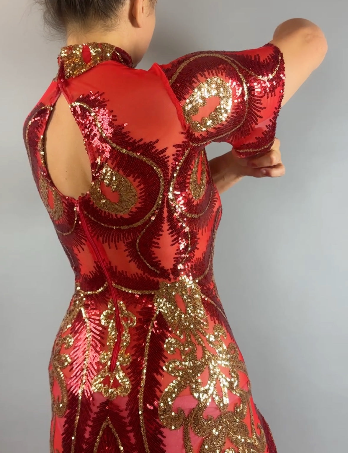 Person wearing the Red And Gold Sequin Sheer Dress with hand accessories, sleeveless, adjusting their sleeve and shown from the back.