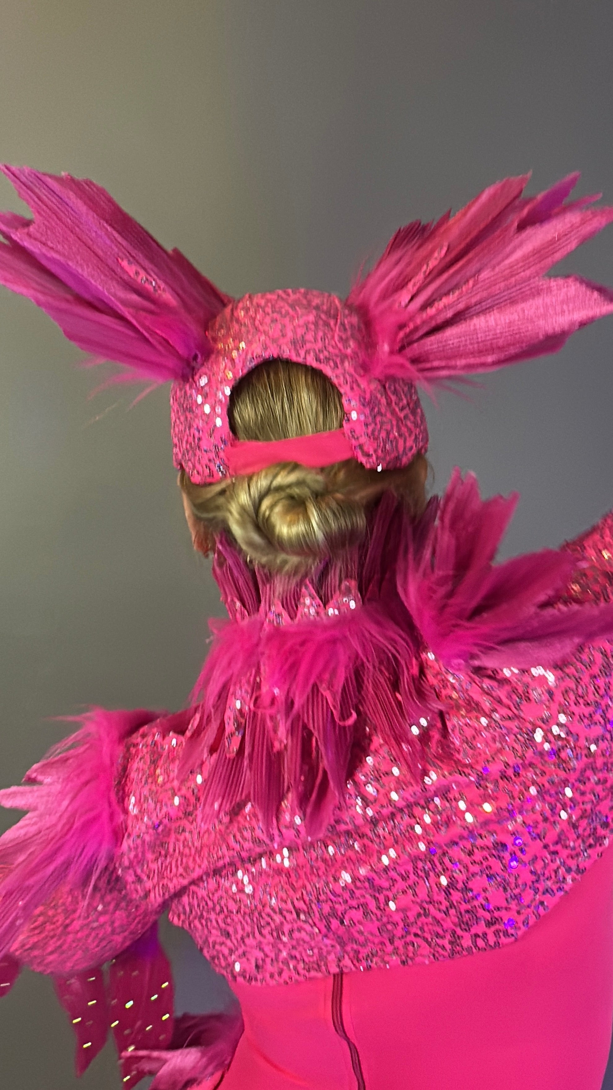 Person wearing the Pink Bird full costume for aerial and dancers, featuring pink glittery fabric, feathered details, and a matching headpiece, shown from behind.