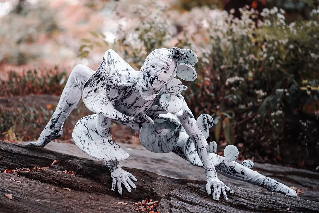 A person wearing the Mushroom Fungus Costume—futuristic fashion and trending exotic dance wear—crouches on a rock in a forested area.