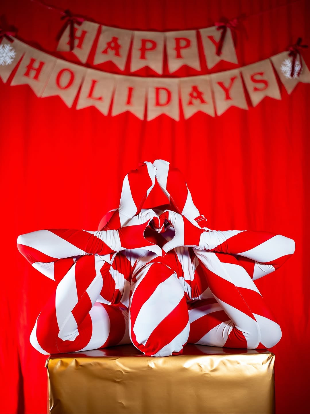 Three people in Candy Cane Bodysuit, Turtleneck, Full Sleeves pose in a star shape in front of a "Happy Holidays" banner.