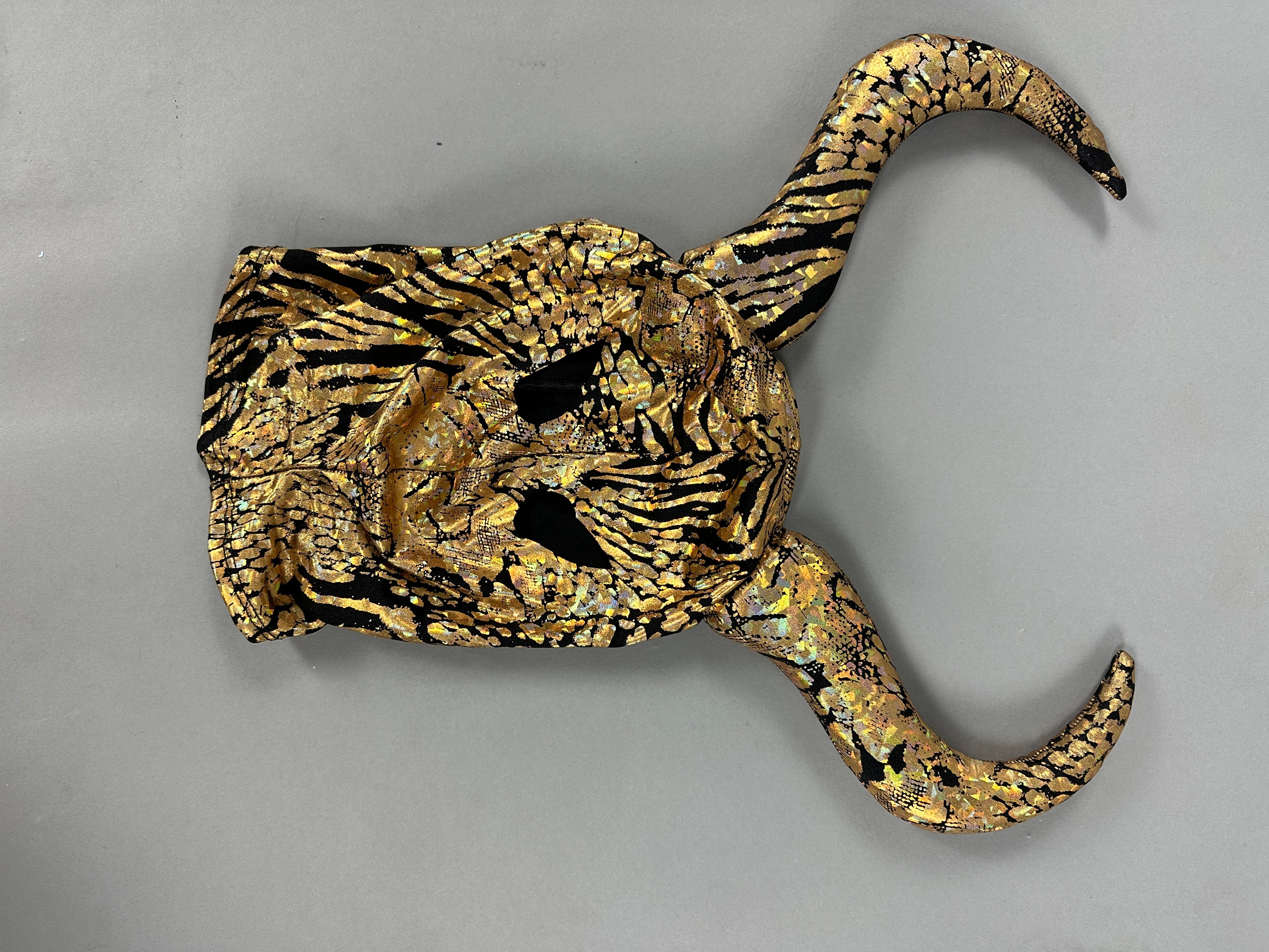 The Gold & Black Gazelle Creature Costume features a mask with elegantly curved horns, reminiscent of a gazelle headdress against a gray backdrop.