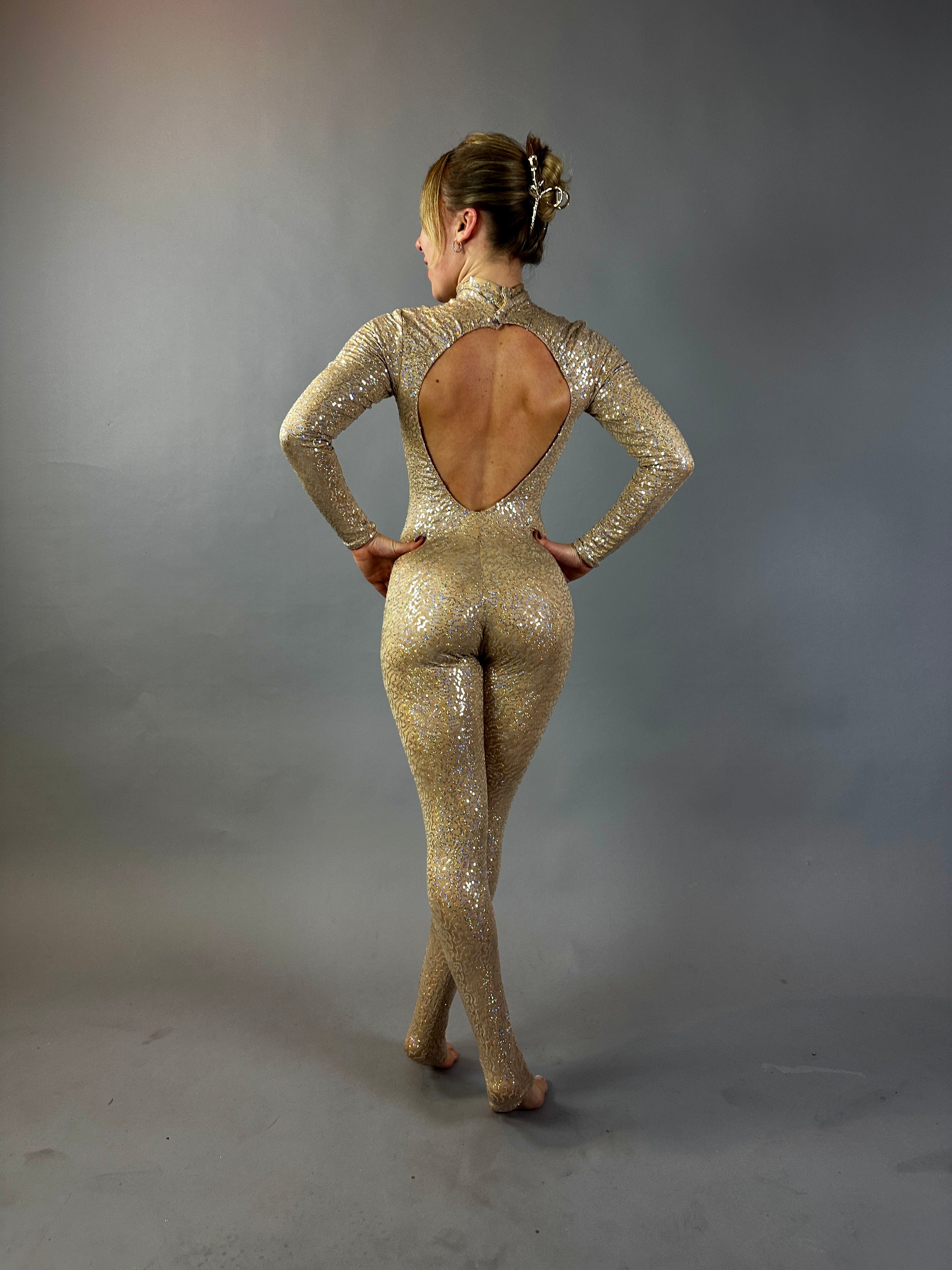 A woman in a Champagne Fairy Sequin Catsuit with an open back and turtleneck stands in a studio with a gray backdrop, the sparkly performance costume&