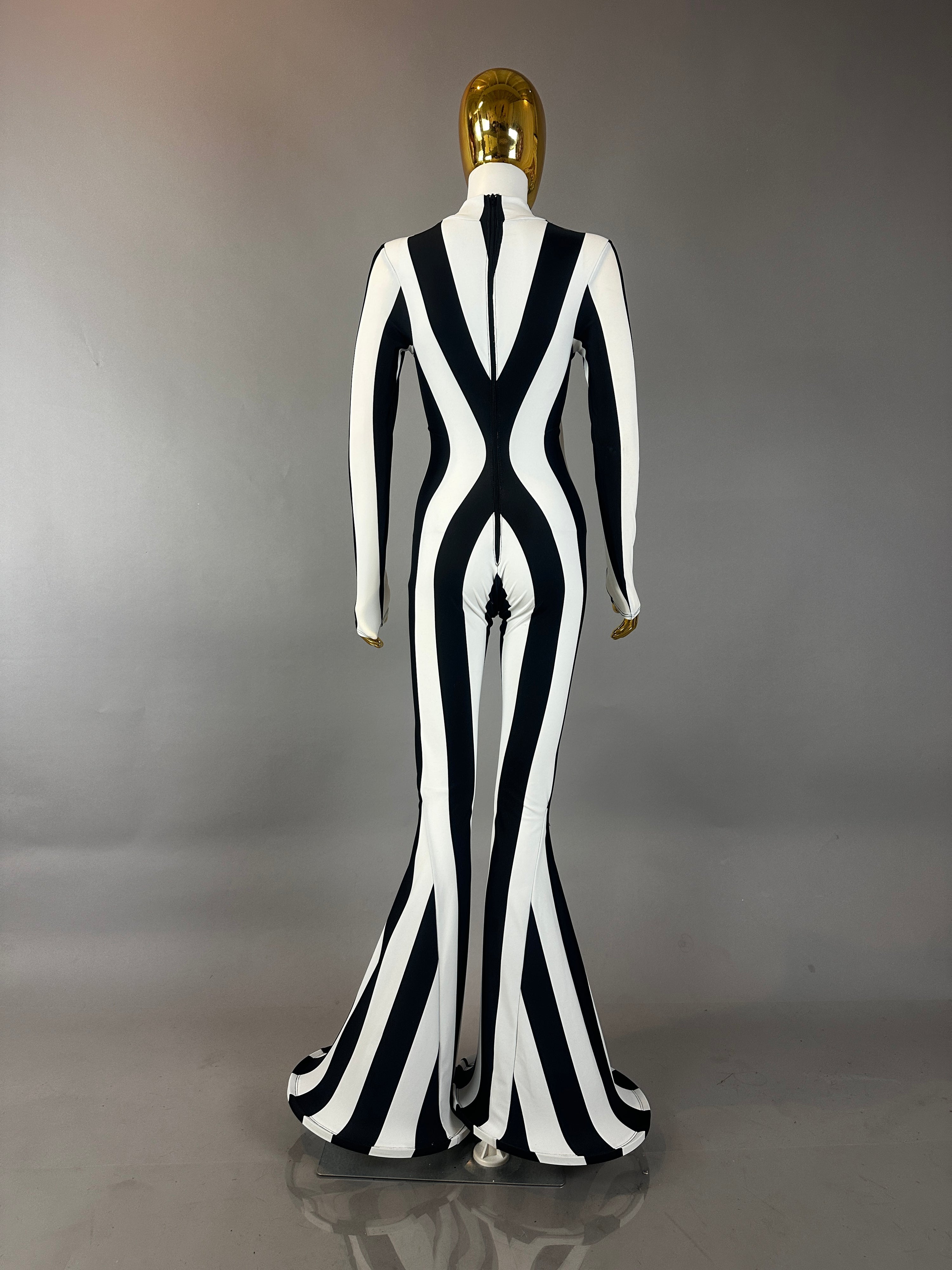 Model wears the Rave White Striped Catsuit with bellbottom legs, featuring bold black and white stripesāan eye-catching festival performer costume, shown from the back against a gray background.