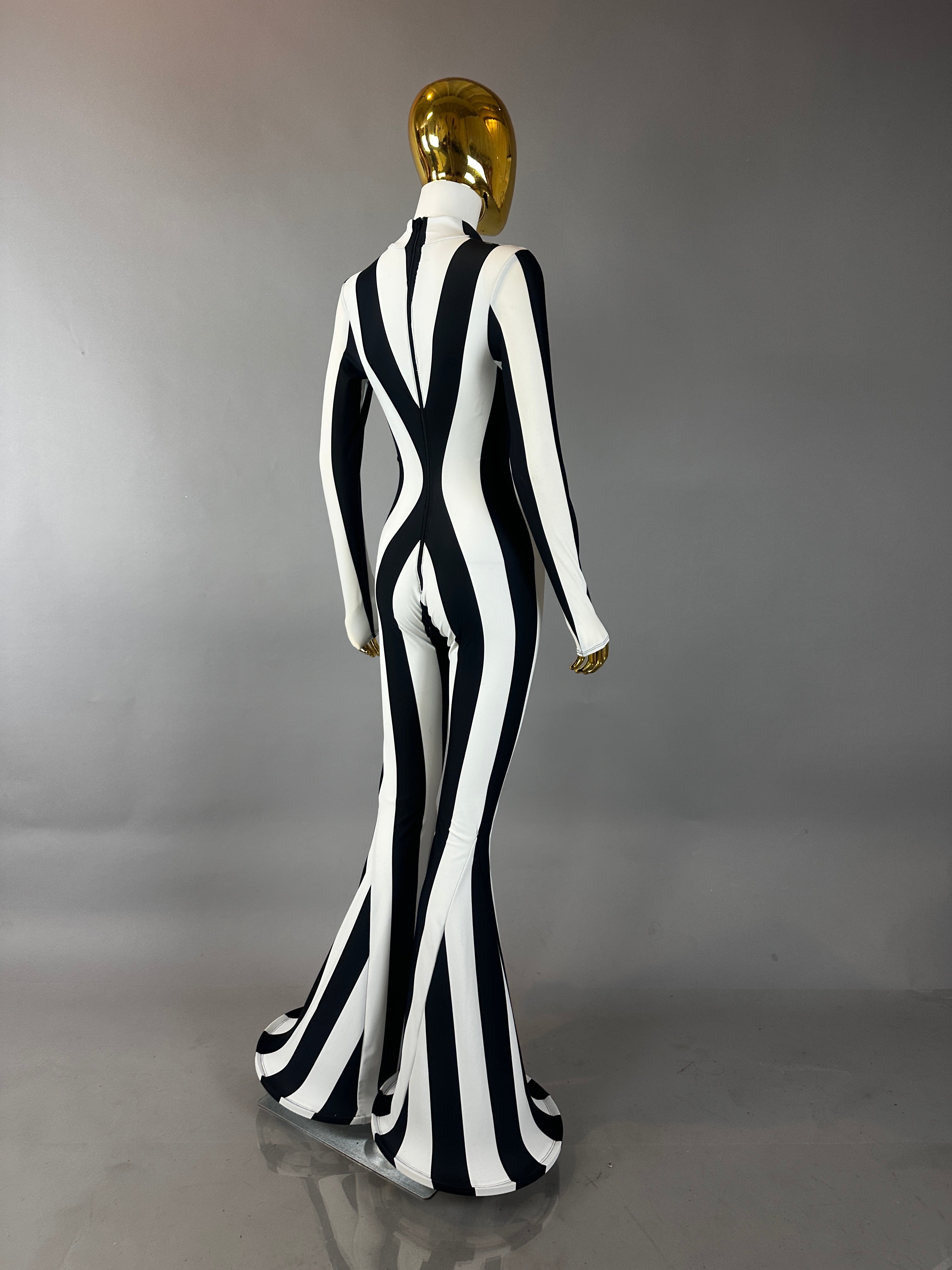 A mannequin models the Rave White Striped Catsuit with bellbottom legs, standing against a gray background—a bold festival performer outfit.