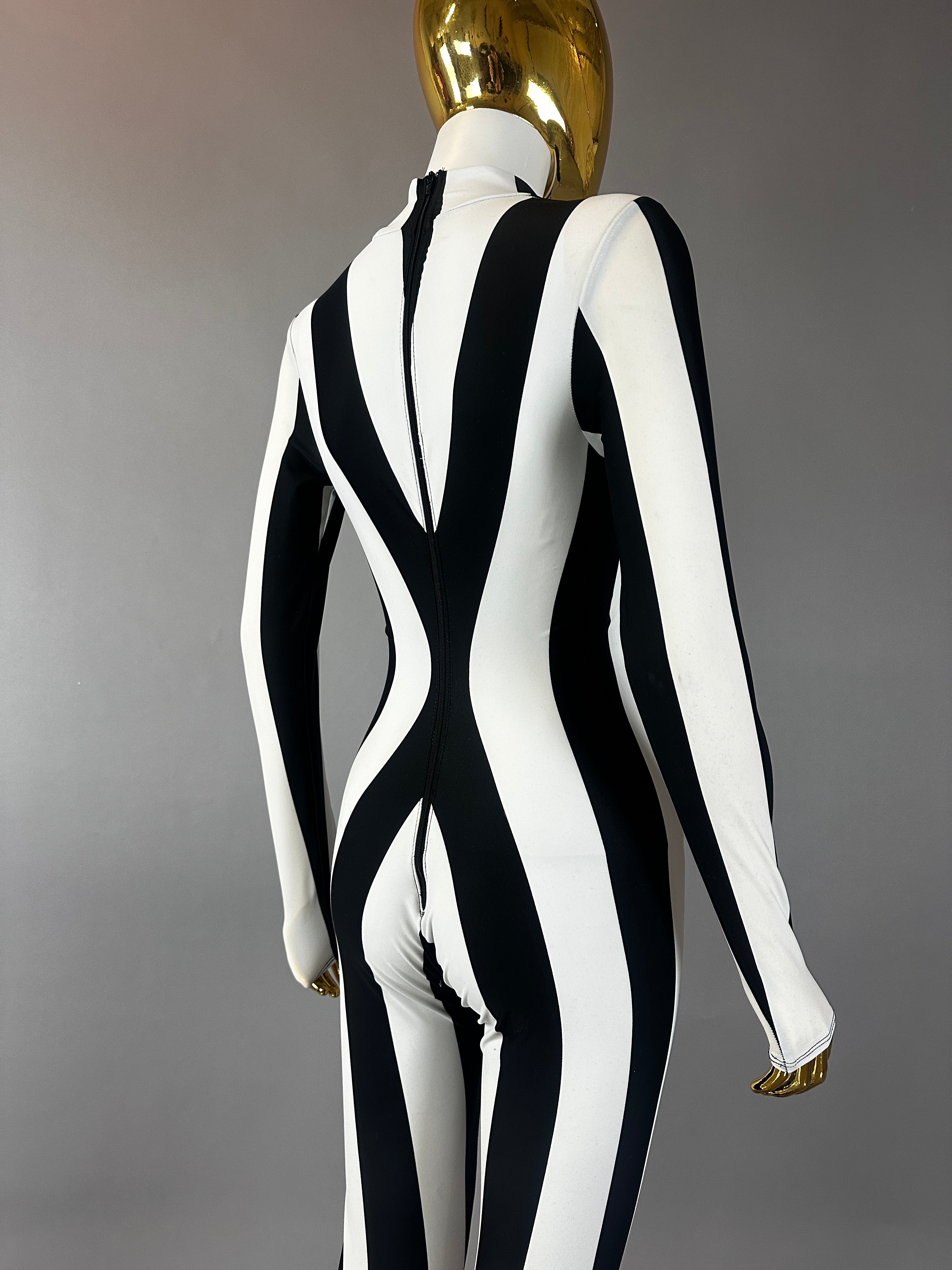A mannequin models the Rave White Striped Catsuit with bellbottom legs—an eye-catching, fitted black and white festival performer outfit—set against a gray background.
