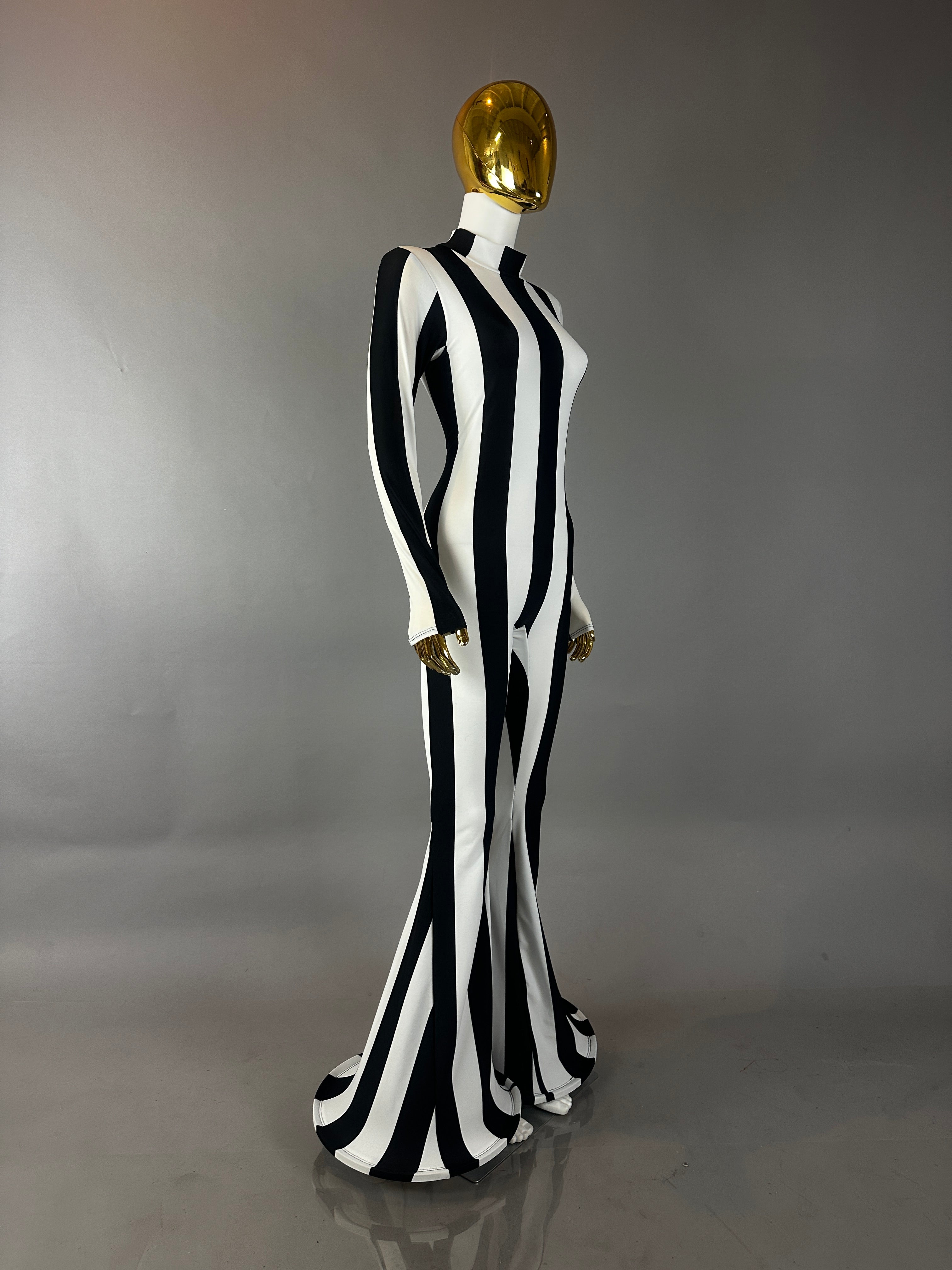 A gold mannequin wears the Rave White Striped Catsuit with bellbottom legs, featuring bold black and white stripes—ideal for performance costumes—posed against a gray background.