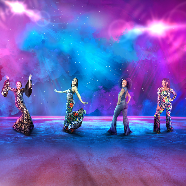 Four women in colorful, retro outfits pose under bright lights on a vibrant, neon-lit stage.