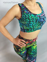 A person stands confidently, hands on hips, wearing vibrant Peacock Leggings and Top activewear adorned with a stunning peacock feather design—perfect for yoga fashion and exotic dance wear, trending now.