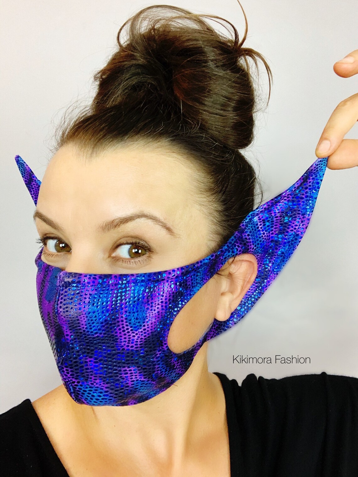 Woman wears the Elf Ears Face Mask for All Ages, a reusable Mandalorian Baby Yoda costume mask with pointed ears, holding one ear out.