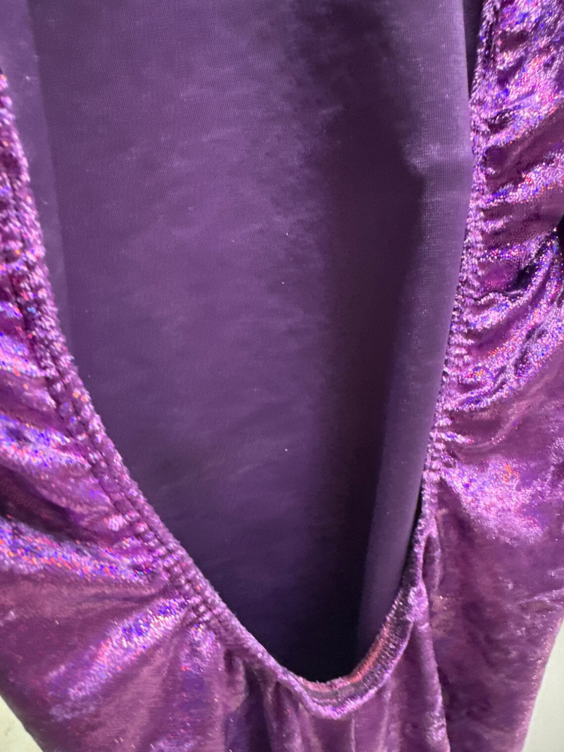 Close-up of shiny, ruched purple fabric from the Velvet Open Back Jumpsuit—exotic dance wear and trending festival outfit—set against a smooth purple background.