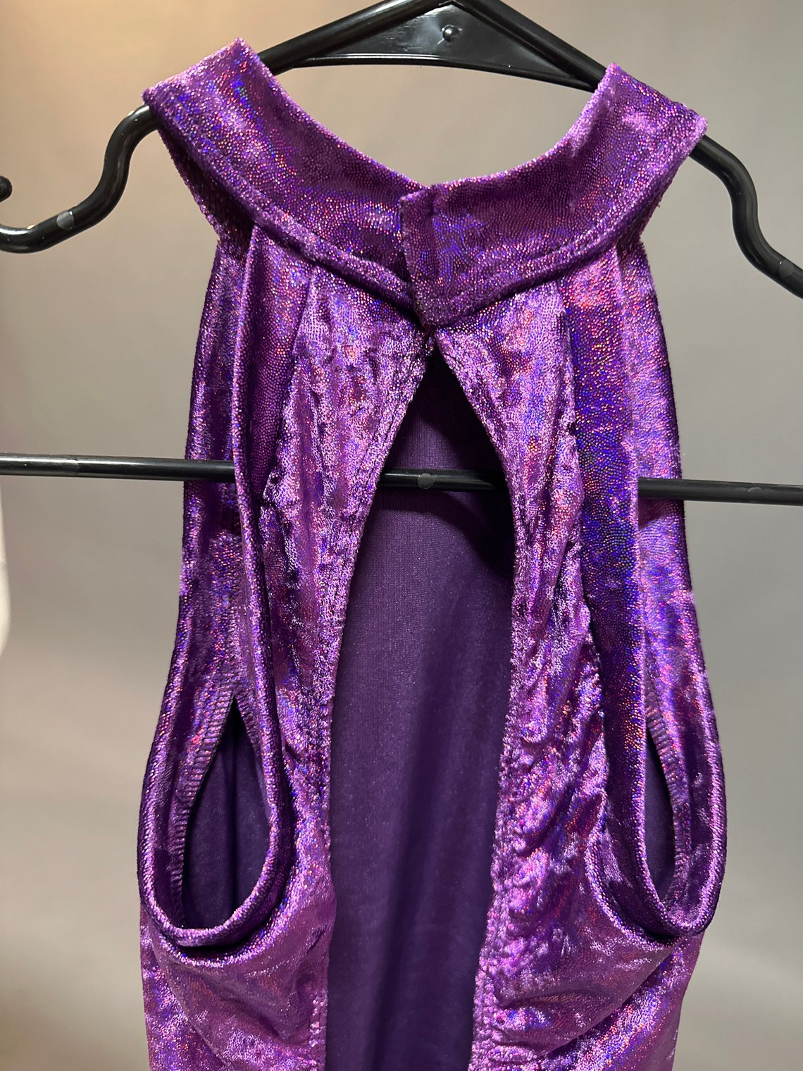 The Velvet Open Back Jumpsuit, an exotic dance wear trending now and ideal for festival, features a sleeveless, shimmering purple velvet design with a keyhole back, displayed on a black hanger.