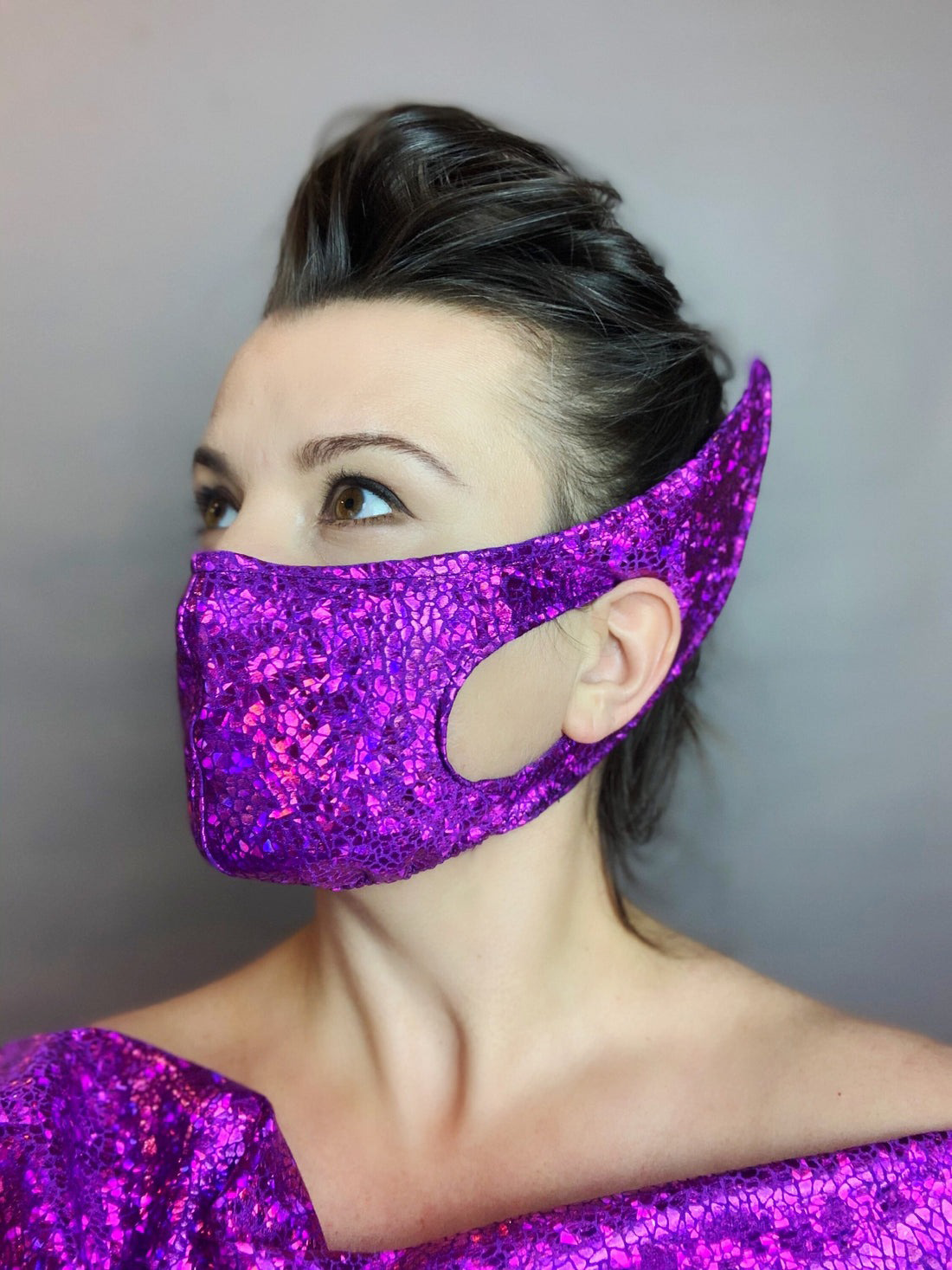 Person wearing the Elf Ears Face Mask for All Ages and matching Beautiful Futuristic Clothing, a reusable elf mask inspired by Mandalorian Baby Yoda, looking to the side in a shiny, textured purple lycra outfit.