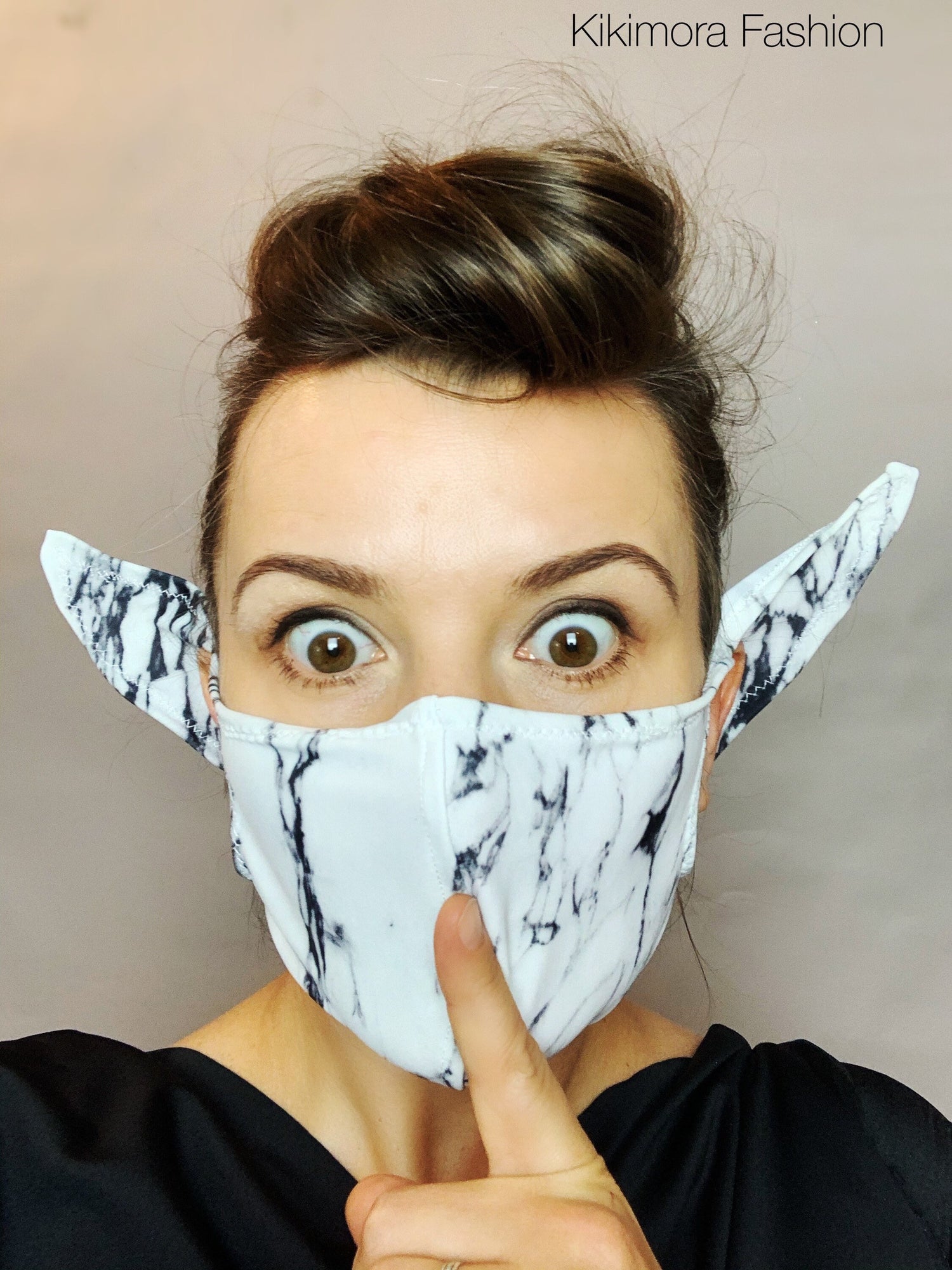A woman wears the Face Mask, Elf Ears Cosplay Costume Accessory, Breathing Face Mask and holds a finger to her lips in a shushing gesture.
