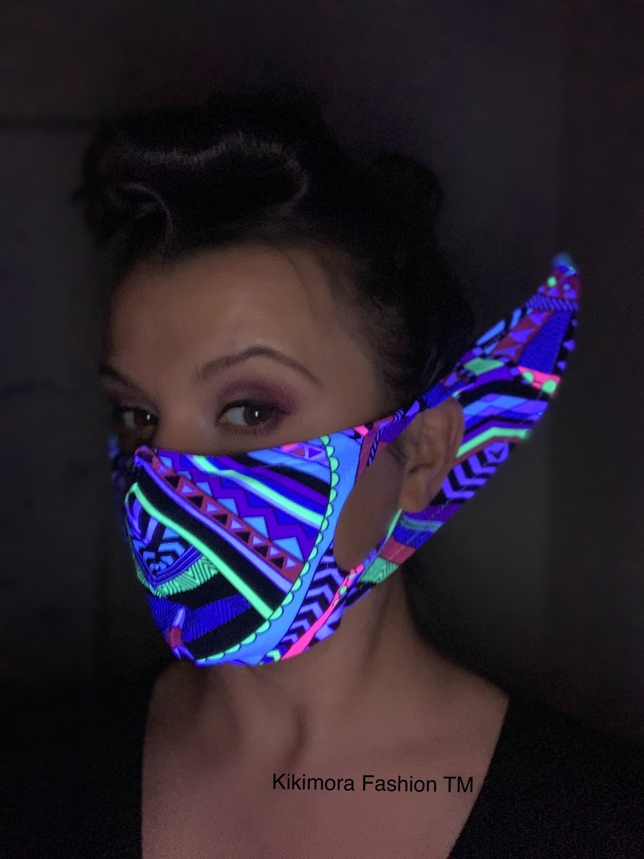 Woman wears a neon geometric Glow Face Mask With 5 Layer HEPA Filter, glowing under blacklightâa bold fashion accessory by Kikimora Fashion that blends unique style with sustainability.