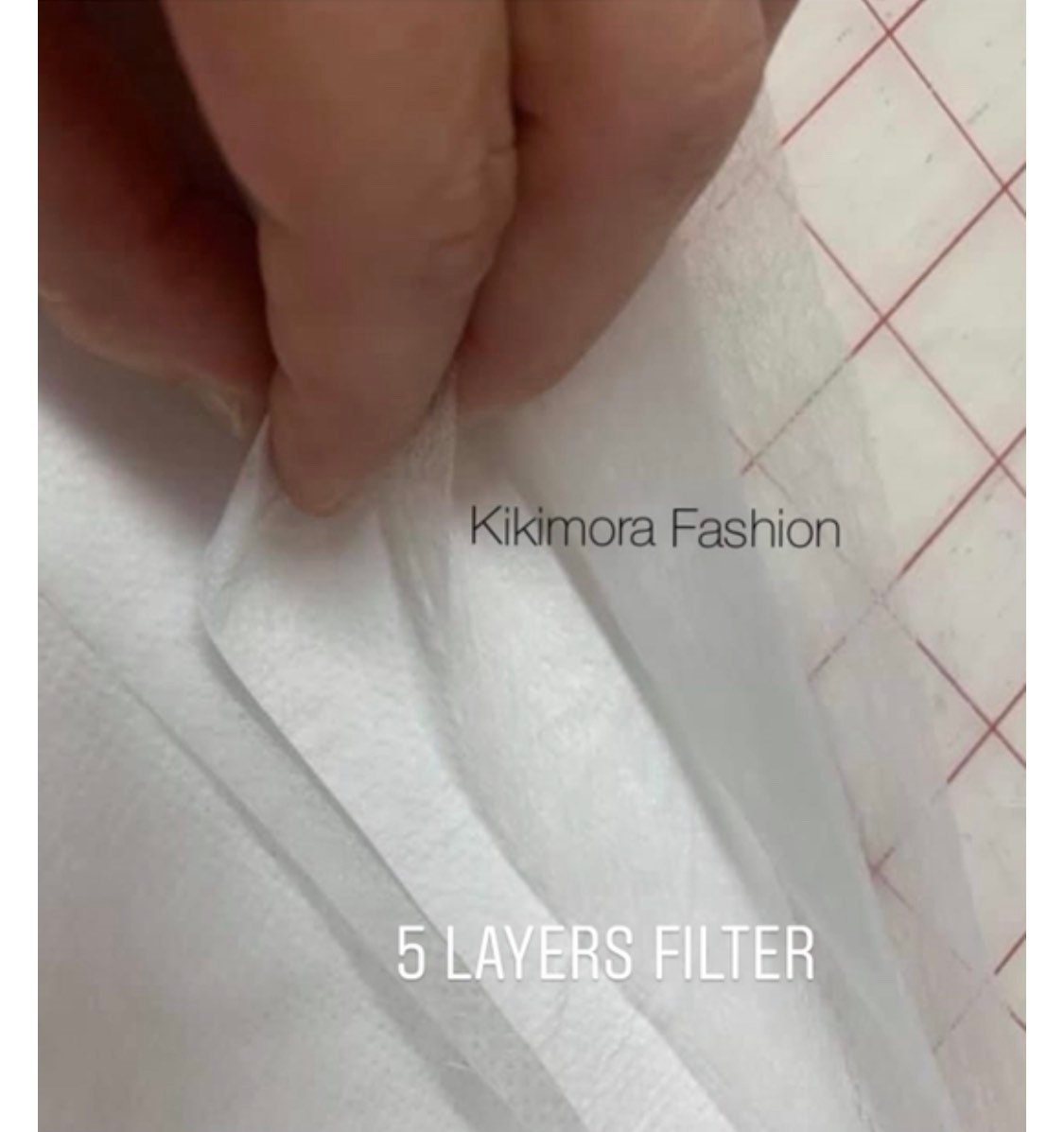 A hand separates layers of white fabric labeled â5 layers filterâ from the Glow Face Mask With 5 Layer HEPA Filter, a fashion accessory by Kikimora Fashion, highlighting their dedication to sustainable style.