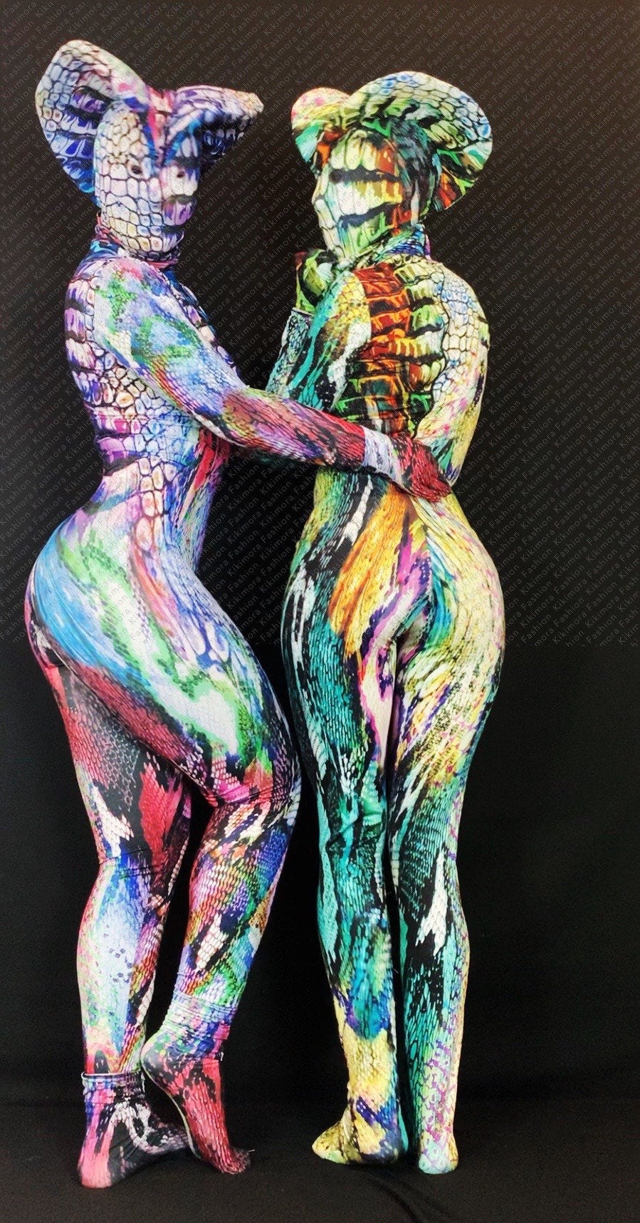 Two figures face each other in vibrant snake print "Fantasy Creature" jumpsuits, made from Lycra and tailored to fit. The Zentai fashion catsuits highlight exotic reptile patterns against a dark background.