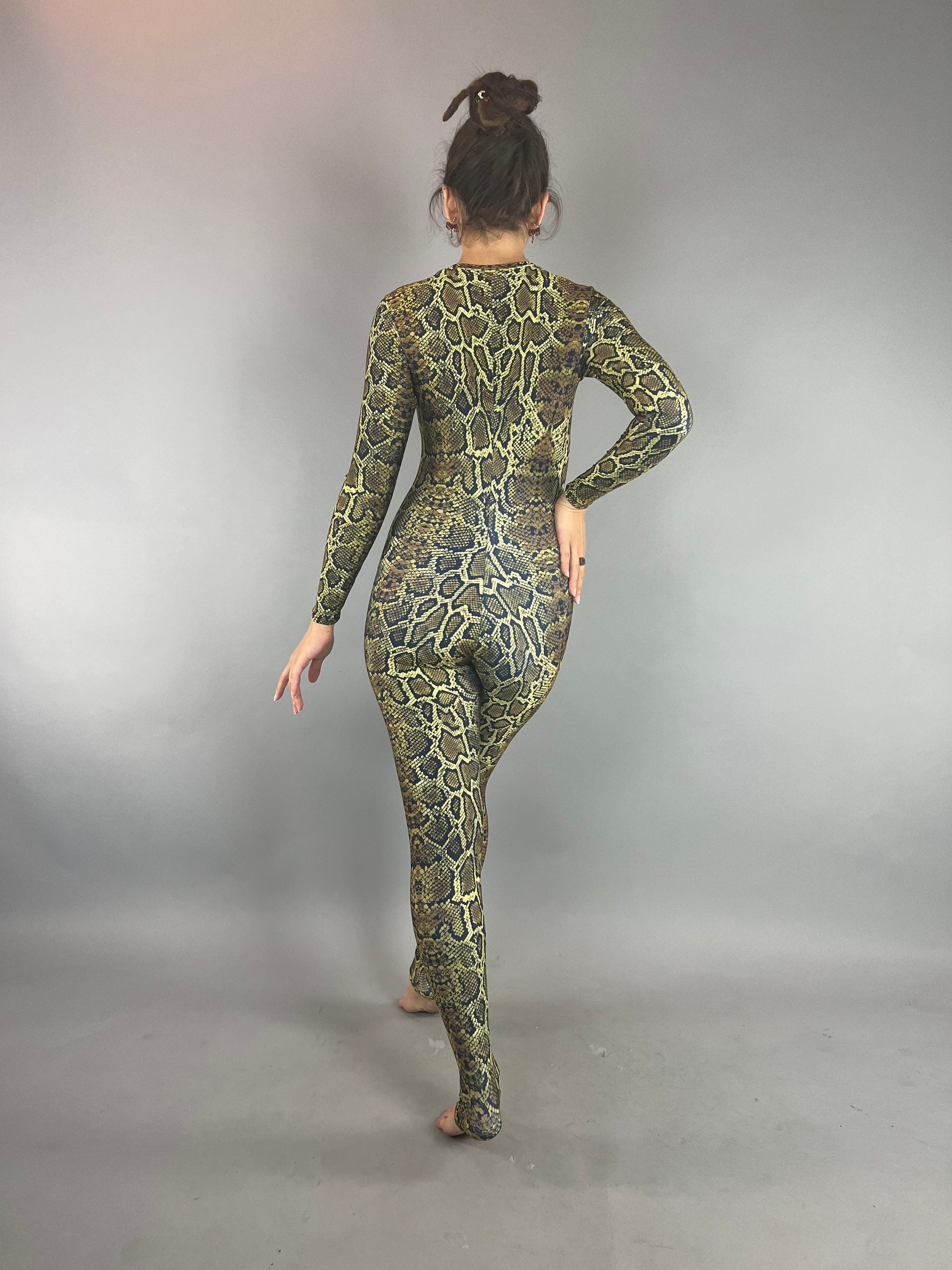 Person faces away, wearing the Beautiful Snake Catsuit—long-sleeve, full-body, with a vivid snakeskin pattern. Perfect for festival fashion, yoga, watersports, or as a trendy UV protective swimsuit. Stands on a gray floor.