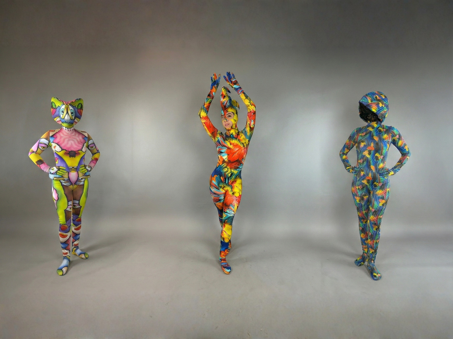 Three people in colorful, full-body painted suits stand posing against a plain gray background.