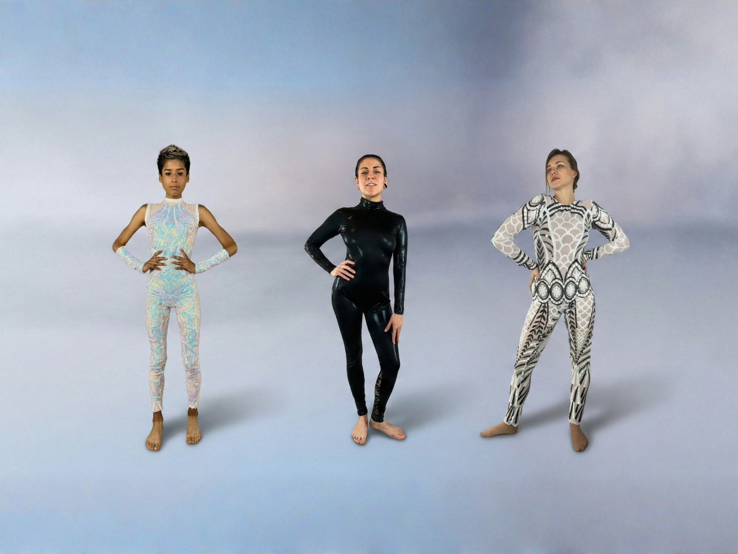 Three people in patterned bodysuits stand barefoot against a light, gradient background, posing confidently.