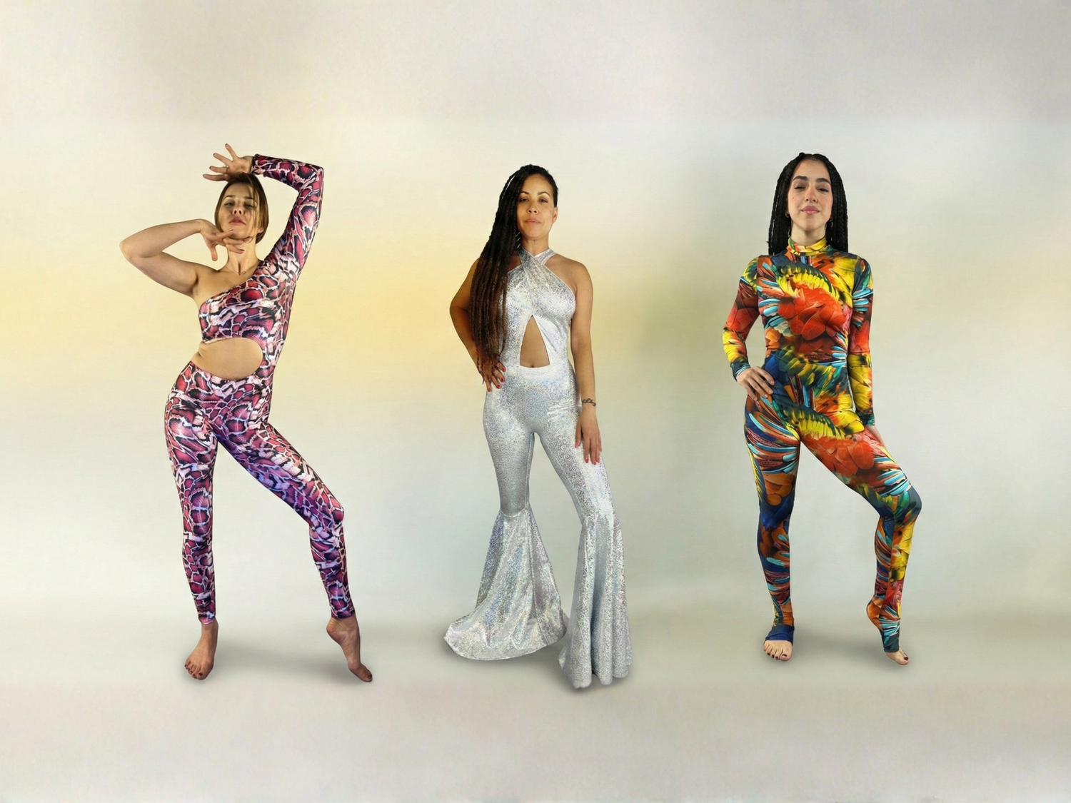 Three women posing in colorful, patterned jumpsuits against a plain, light background.