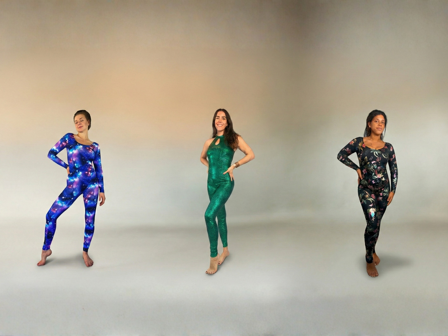 Three women standing in colorful, fitted bodysuits against a plain, gradient background.