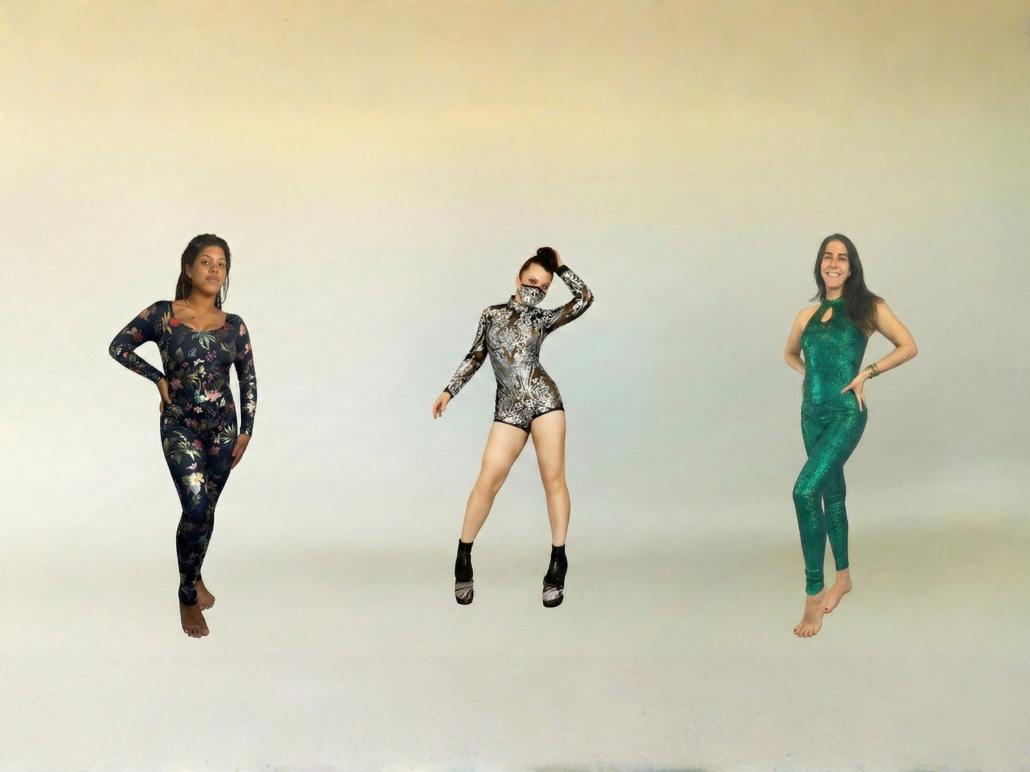 Three women posing in colorful, shiny bodysuits against a light, neutral background.