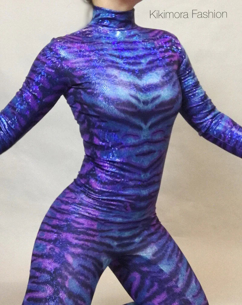 Person wearing a shiny, purple and blue animal print bodysuit against a plain background.