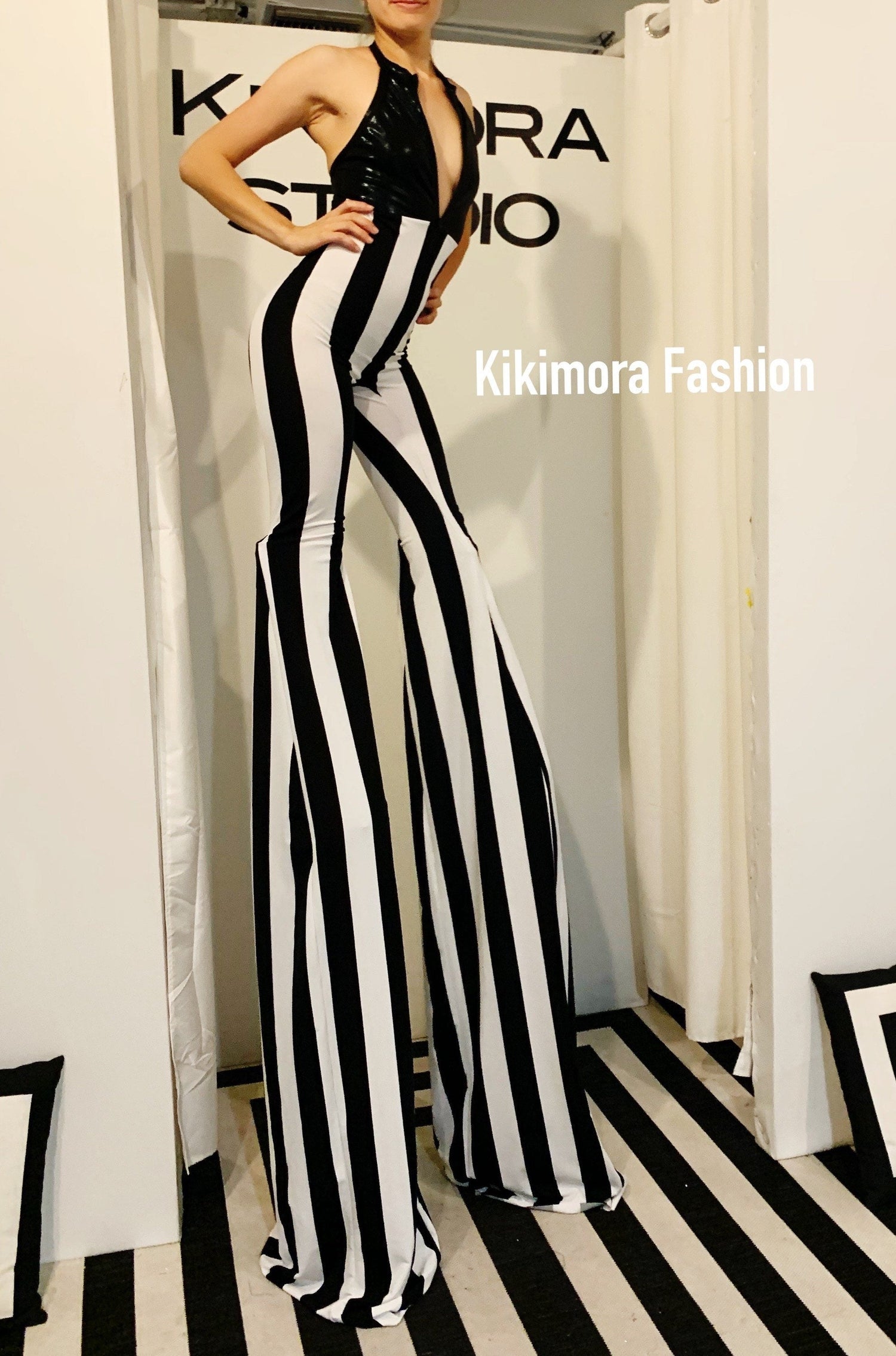 Person wearing black and white striped stilt pants and top stands in front of a sign reading &quot;Kikimora Fashion.