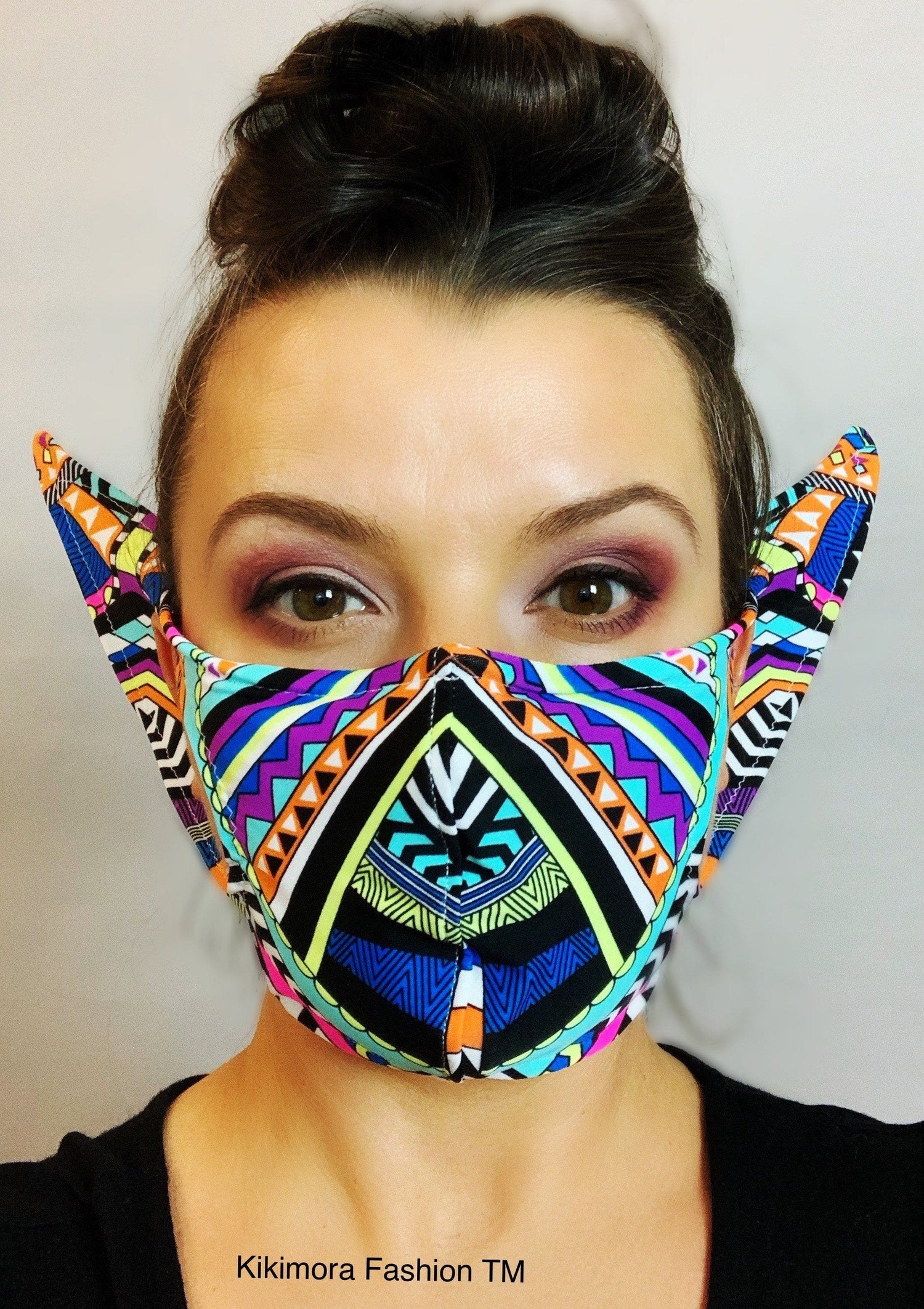 Woman wearing a colorful, geometric-patterned face mask with pointed sides resembling ears.