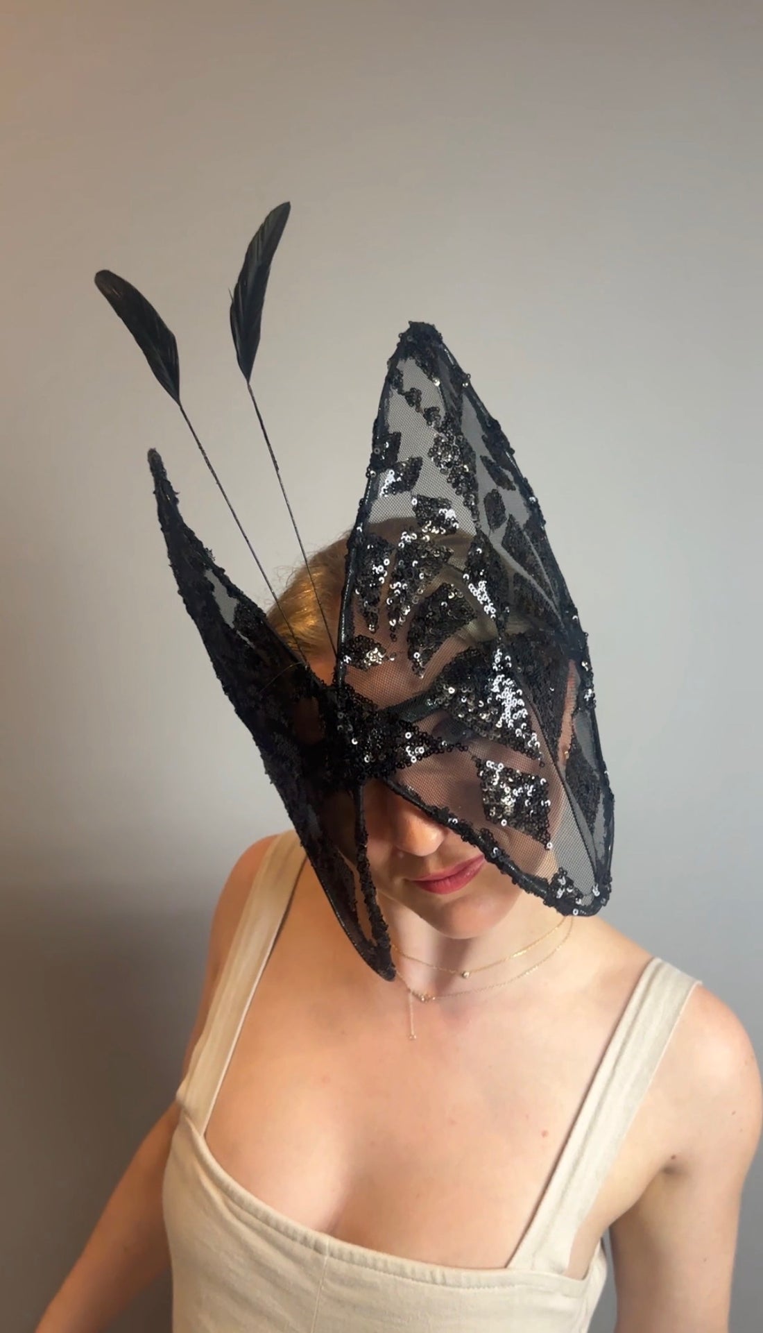 A woman models the Butterfly Headpiece—an open-face black lace hat and festive holiday costume accessory—standing against a plain gray background, blending elegance with unique style.