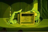 Two performers in Green pixel Cobra Costume Snake Print Catsuits pose by a wooden box on stage, their serpent cosplay bodysuits gleaming under yellow lights.