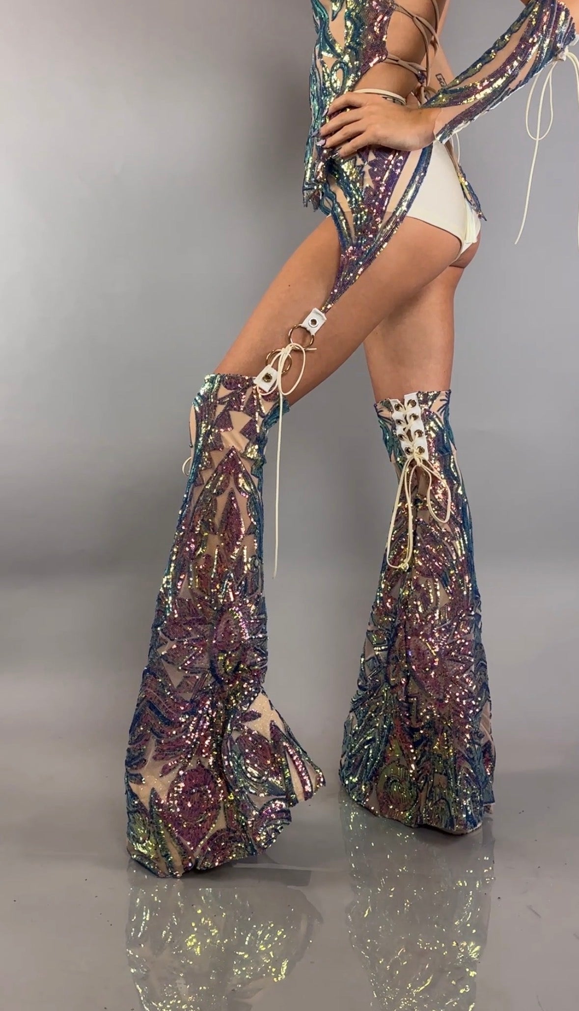 A person wearing the Chaps pants and laced top sequins costume set, a festival outfit featuring sparkly sequin details and leaf patterns, poses against a plain gray background.