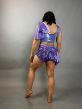 A person stands barefoot facing away, wearing a lavender purple Sequin Dance Costume featuring high waist shorts with half skirt, a crop top, and 4-way stretch mesh.