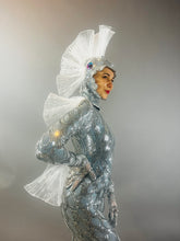 A person wears the Sea Creature—a shiny silver costume featuring fin-like headpiece and back fins—posing against a gray background, showcasing bold couture design.