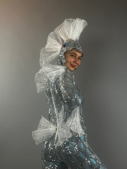 A person smiles, wearing the Sea Creature costume with shimmering, fin-like details against a plain background, showcasing its couture-inspired design.