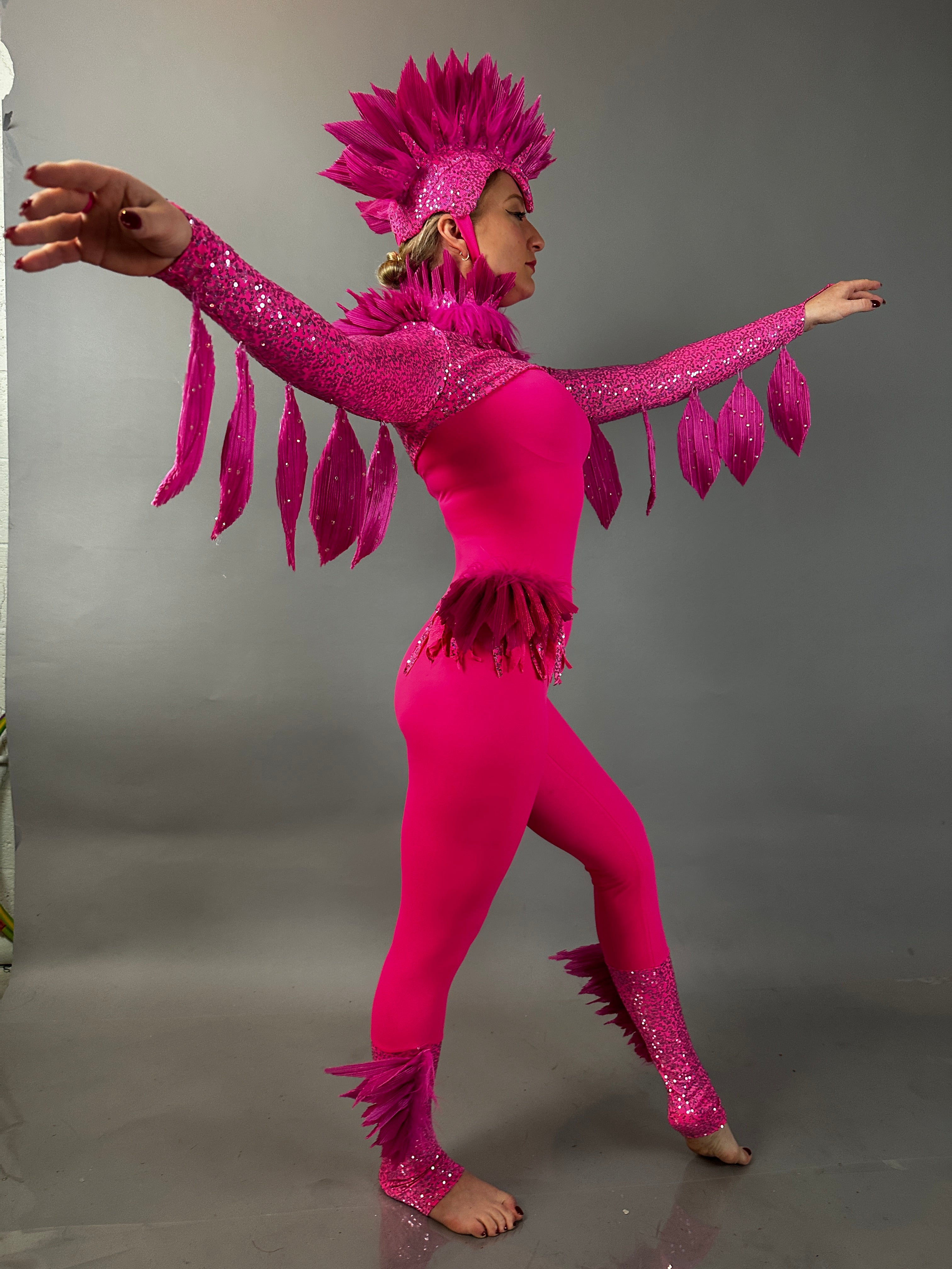 Person in a Pink bird full costume for aerial and dancers poses with arms outstretched against a plain gray background, highlighting the vibrant design of this theatrical show outfit.