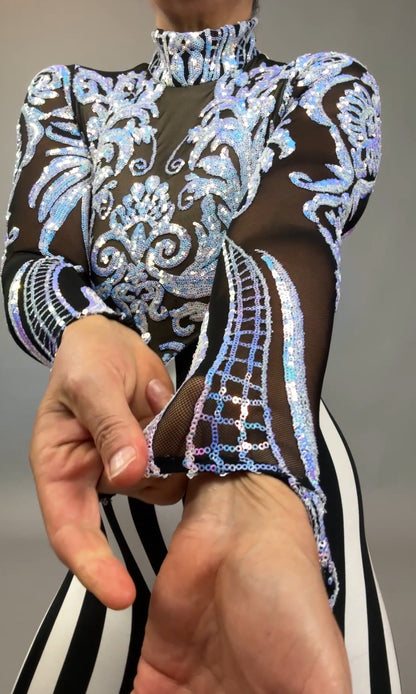 A person pinches the sleeve of the Glamorous sequins Stripes Catsuit, a sheer, patterned costume with blue and silver stripes and a striking sequined leaf design.